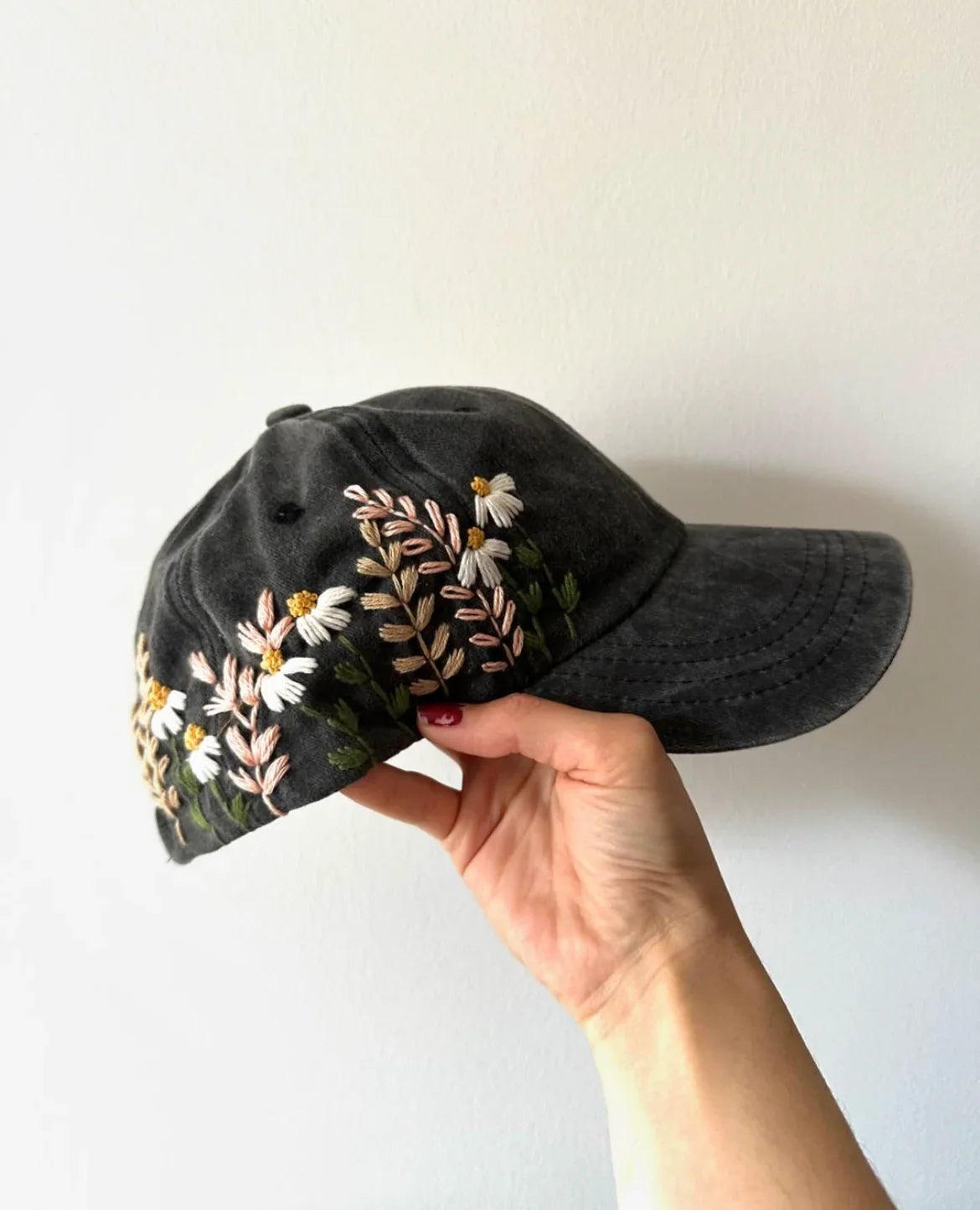 Black denim cap with desaturated floral hand embroidery held against a white background