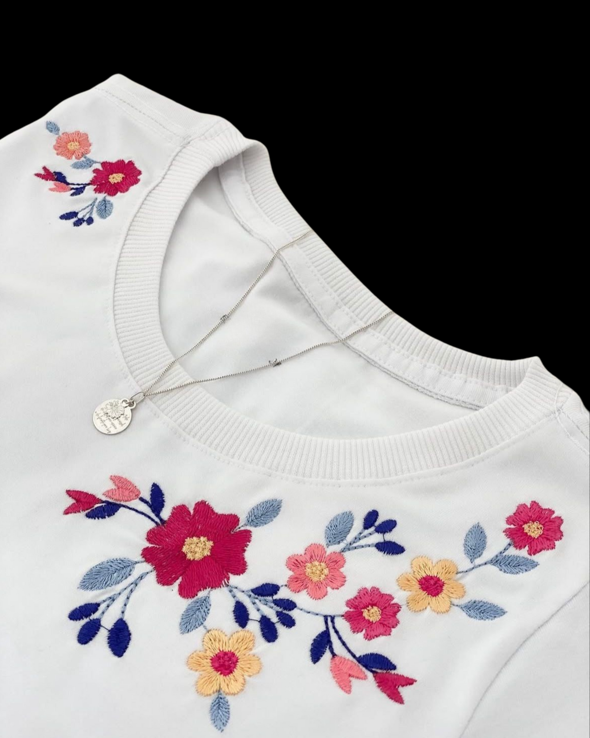 Hand embroidery stitches worked together on a white cotton tee - satin petals, stem-stitch stalks and French-knot centres