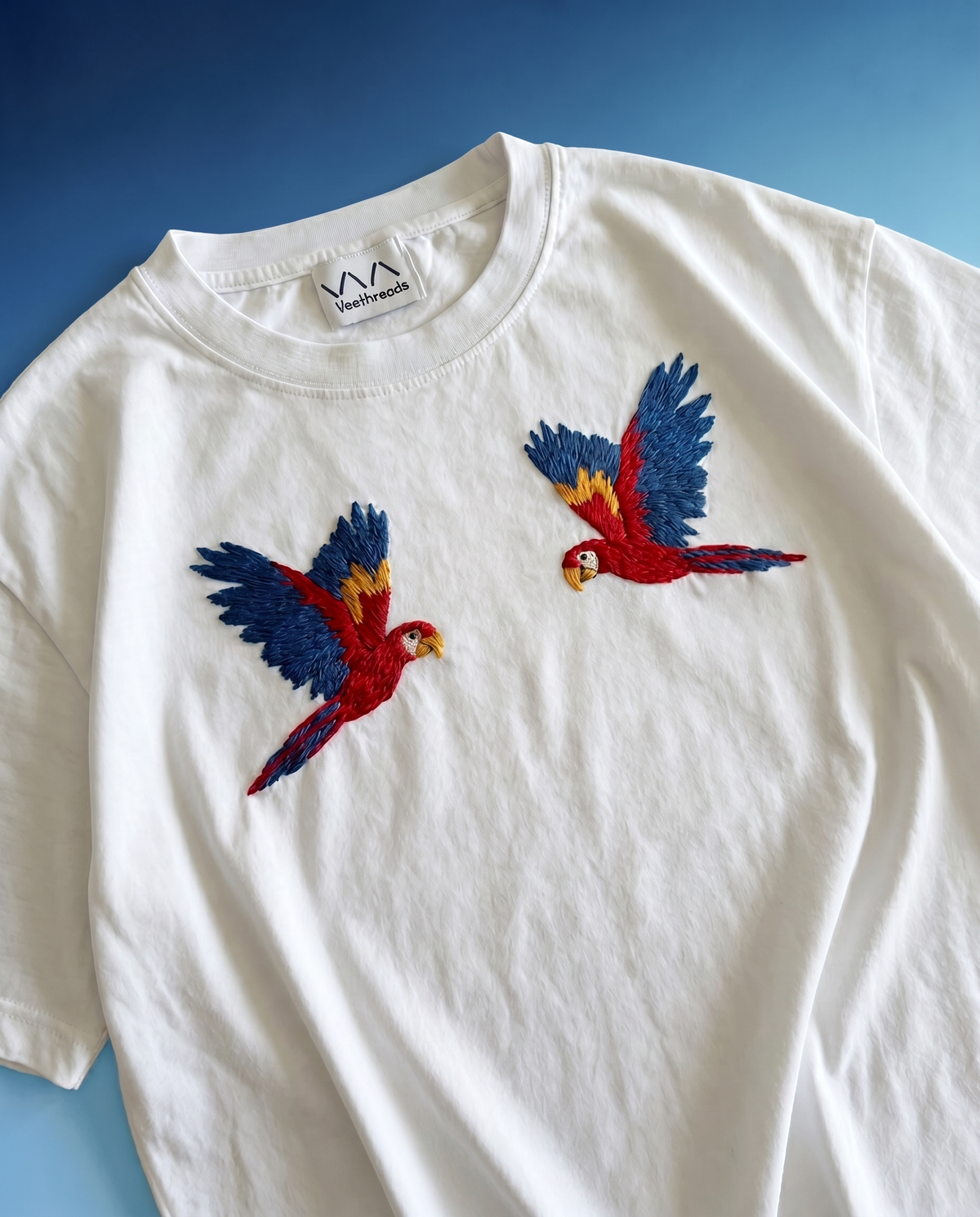 Hand-embroidered scarlet macaw parrot stitched in real thread on a white cotton oversized t-shirt