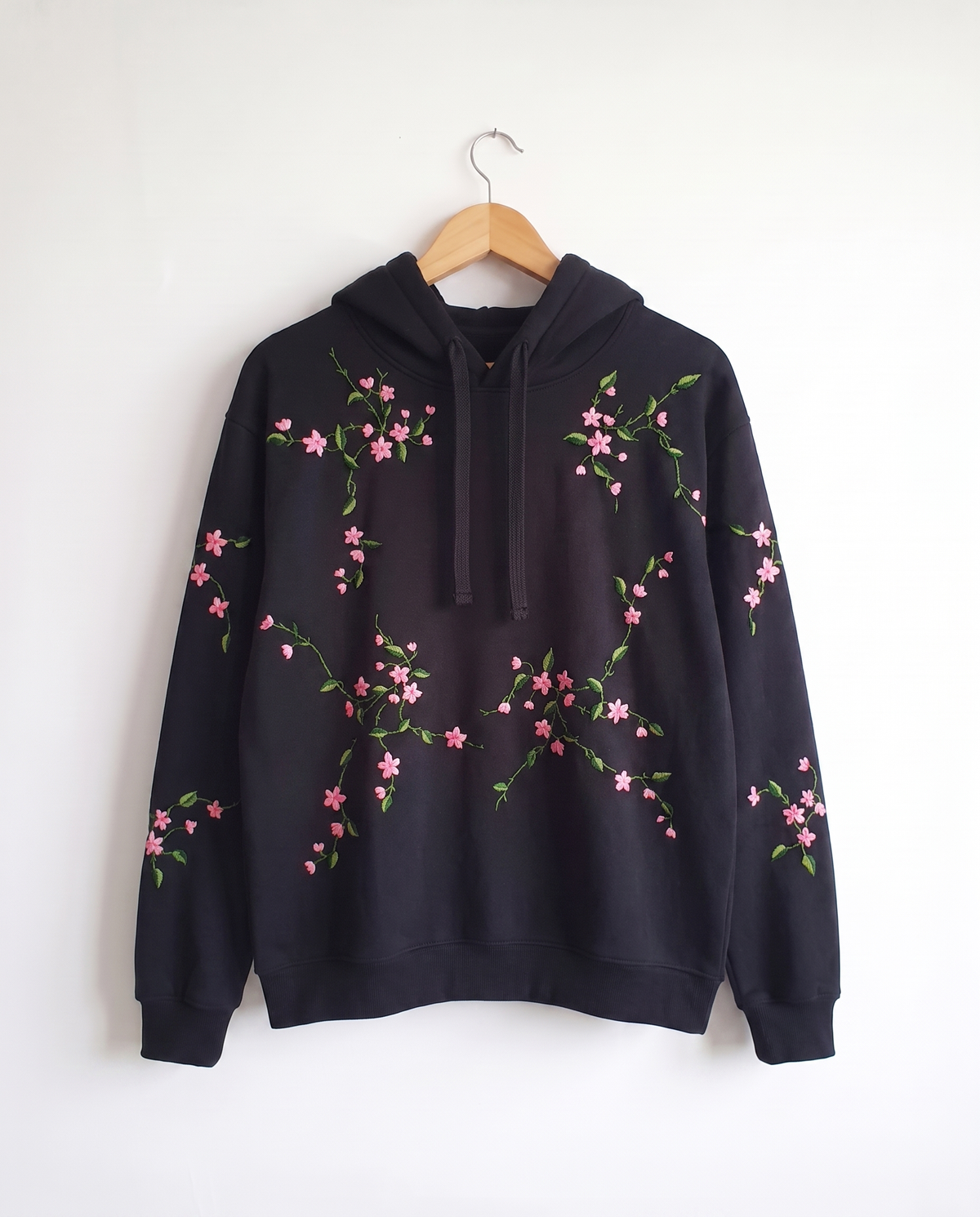 Black cotton fleece hoodie with pink cherry blossom branches hand embroidered across it