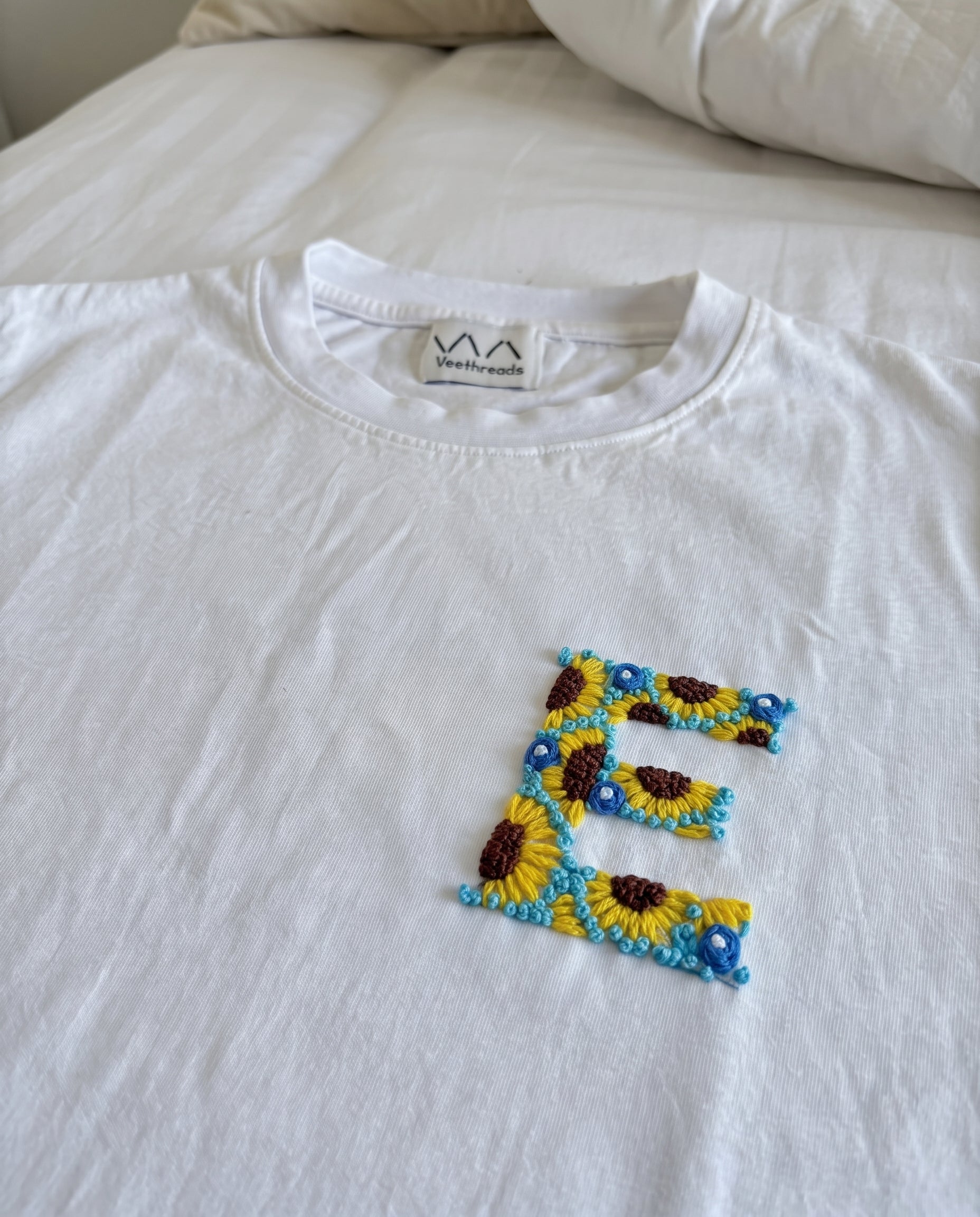 Custom initial stitched from sunflowers and small blue flowers on white cotton, by Vee Threads