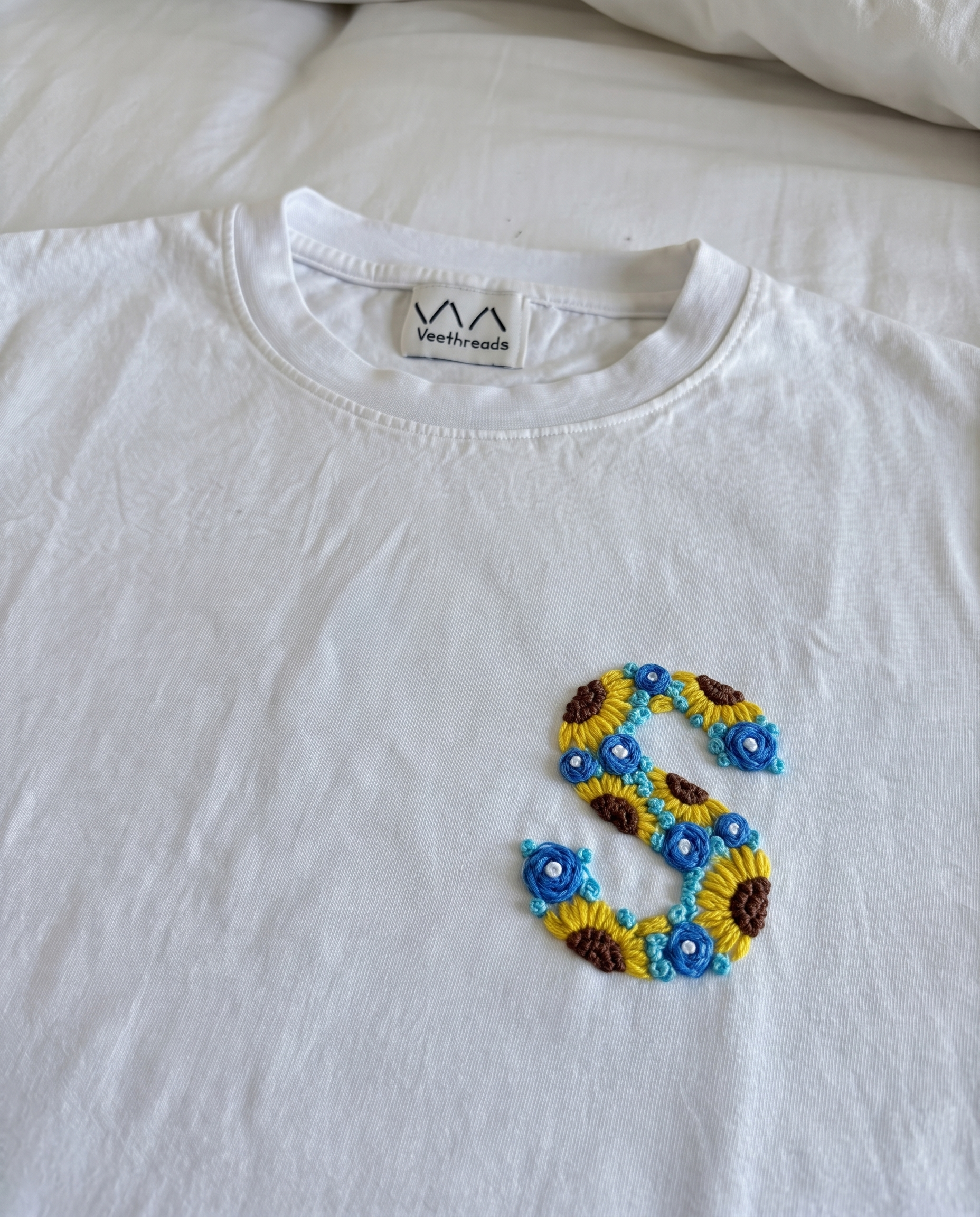 Sunflower and blue-flower hand-embroidered letter on a white cotton tee, by Vee Threads