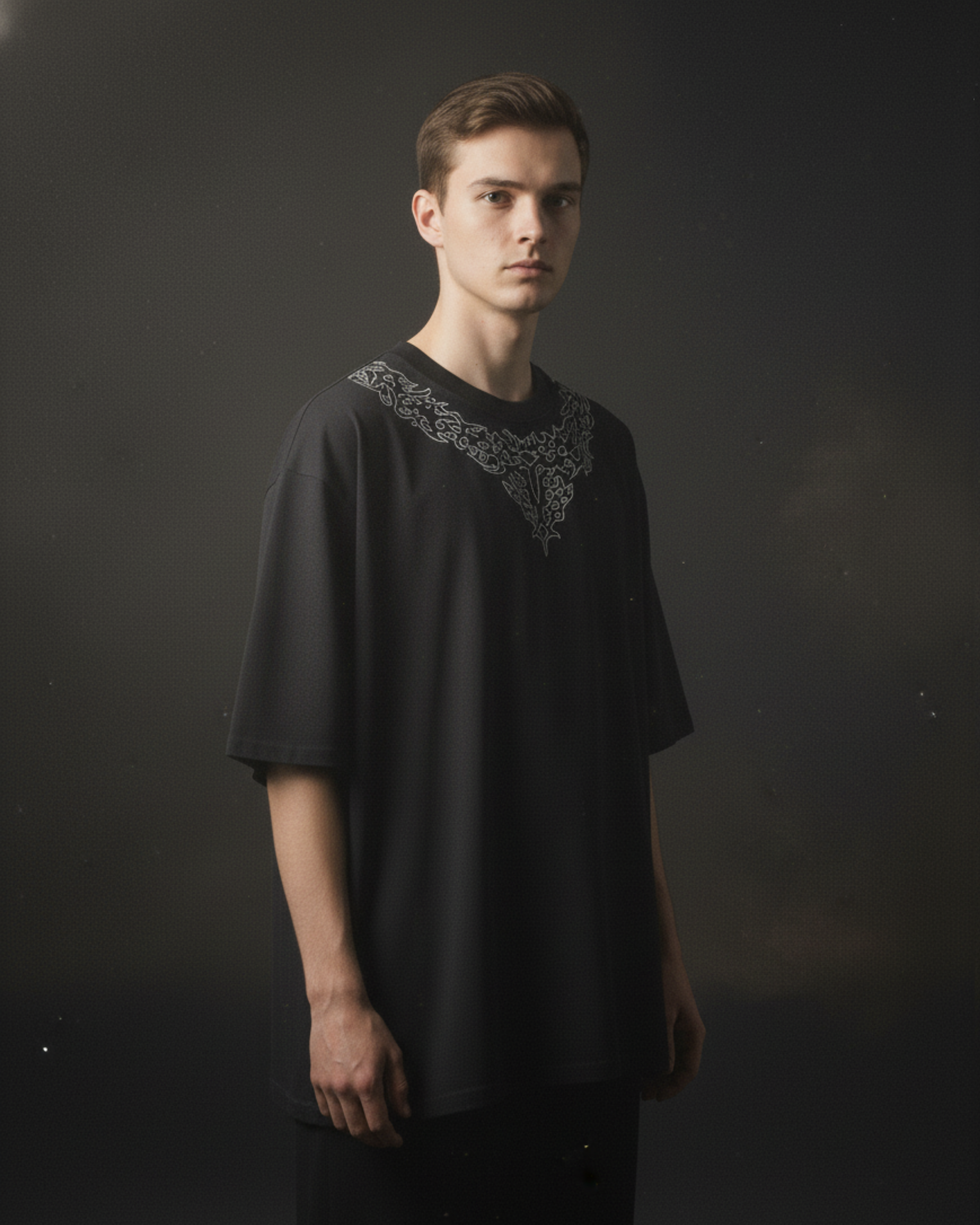 Man wearing a black shirt with intricate embroidery on a dark background