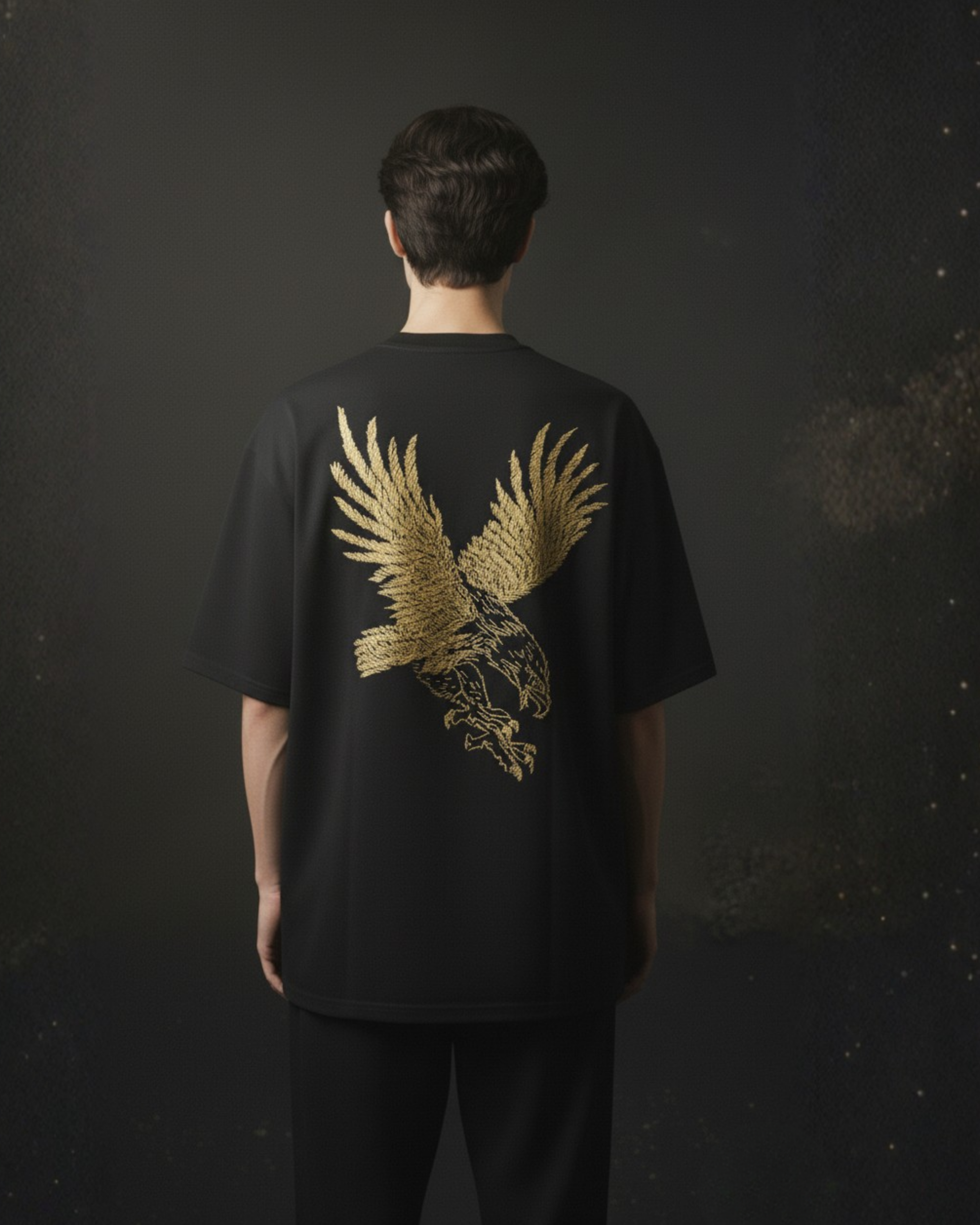 Person wearing a black t-shirt with a gold eagle designhand embroidered on the back against a dark background