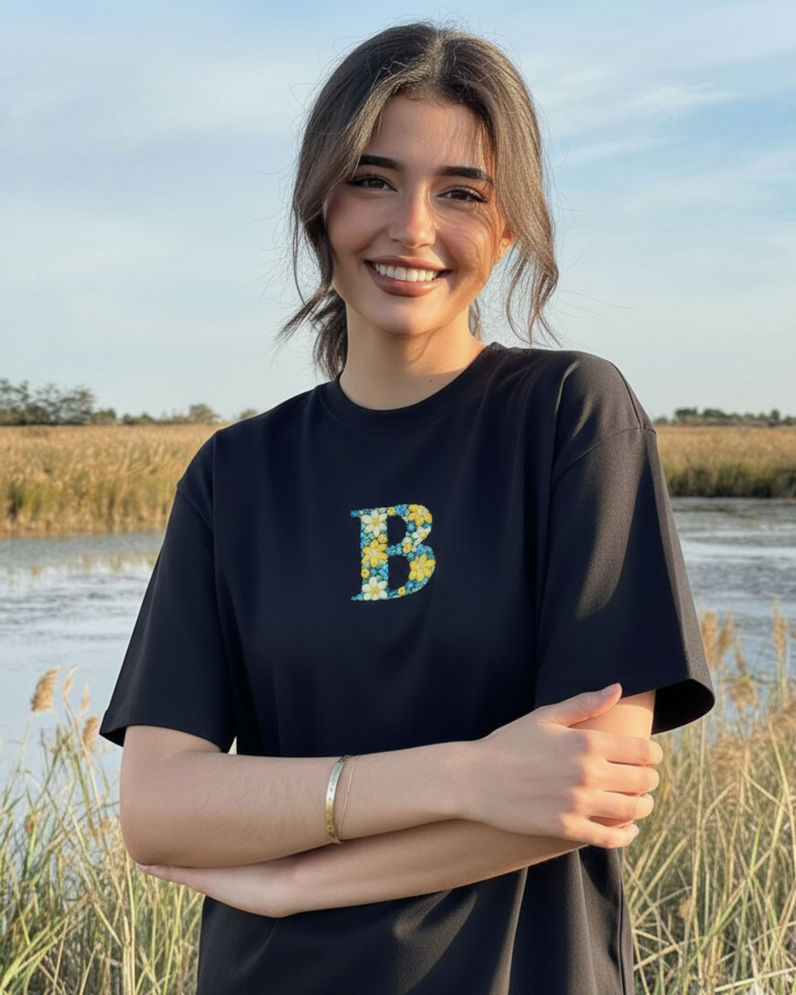 Woman wearing a black t-shirt with a colorful 'B' letter hand embroidered standing in a natural setting.