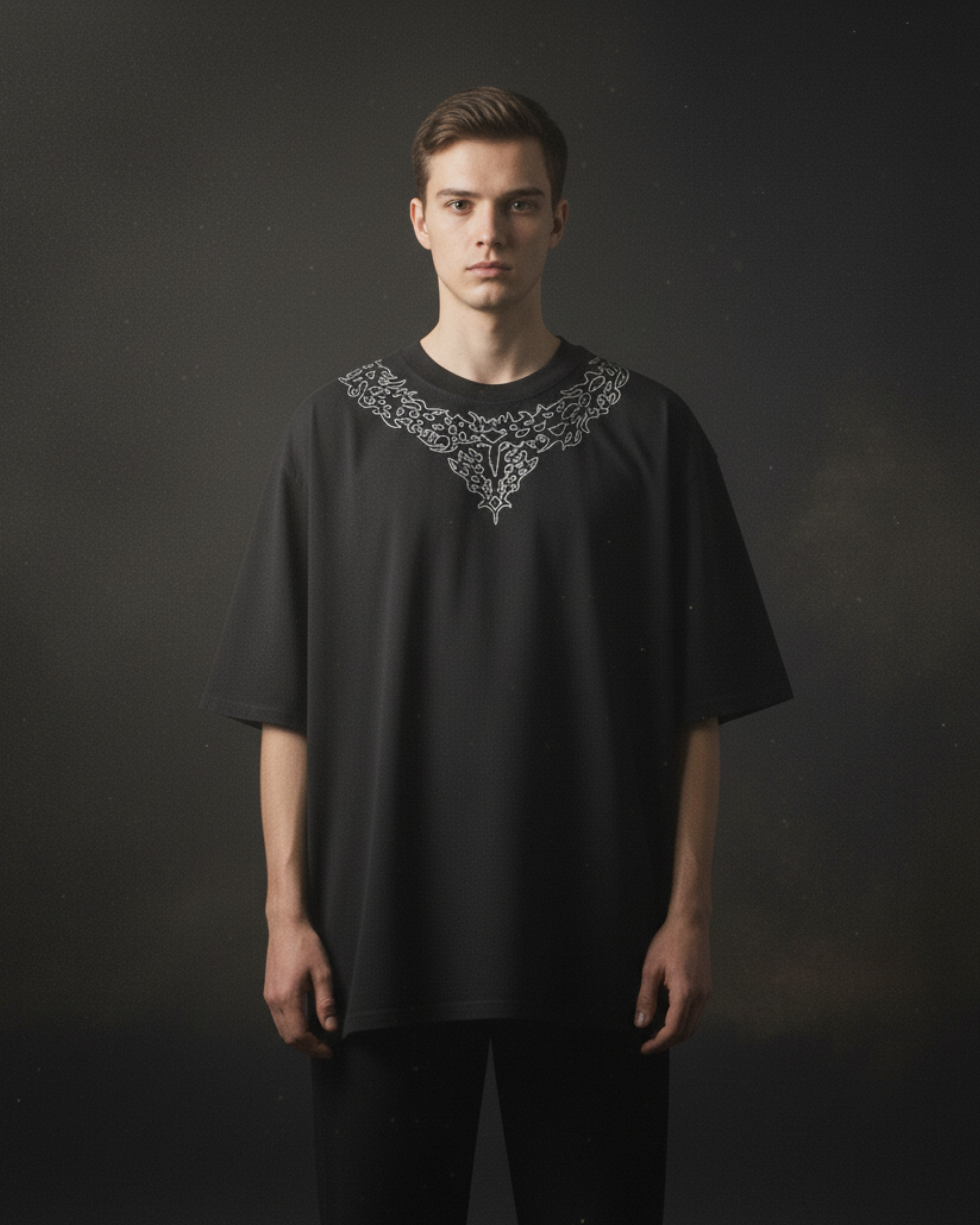 Man wearing a black t-shirt with intricate white embroidery on a dark background