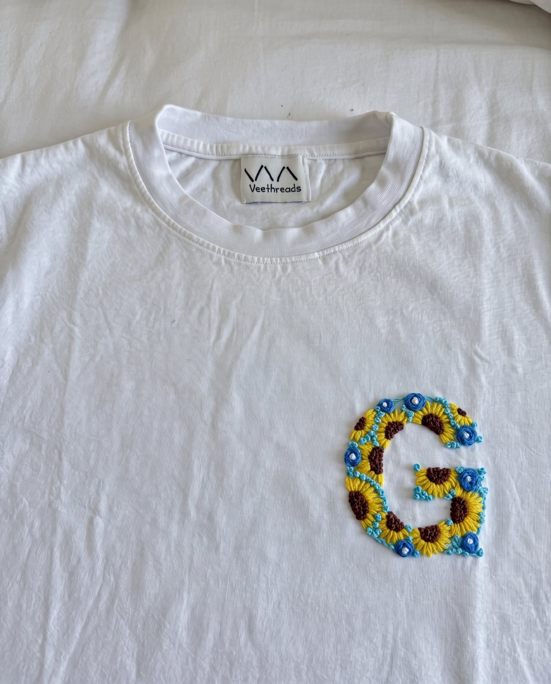 Custom initial stitched from sunflowers and small blue flowers on white cotton, by Vee Threads