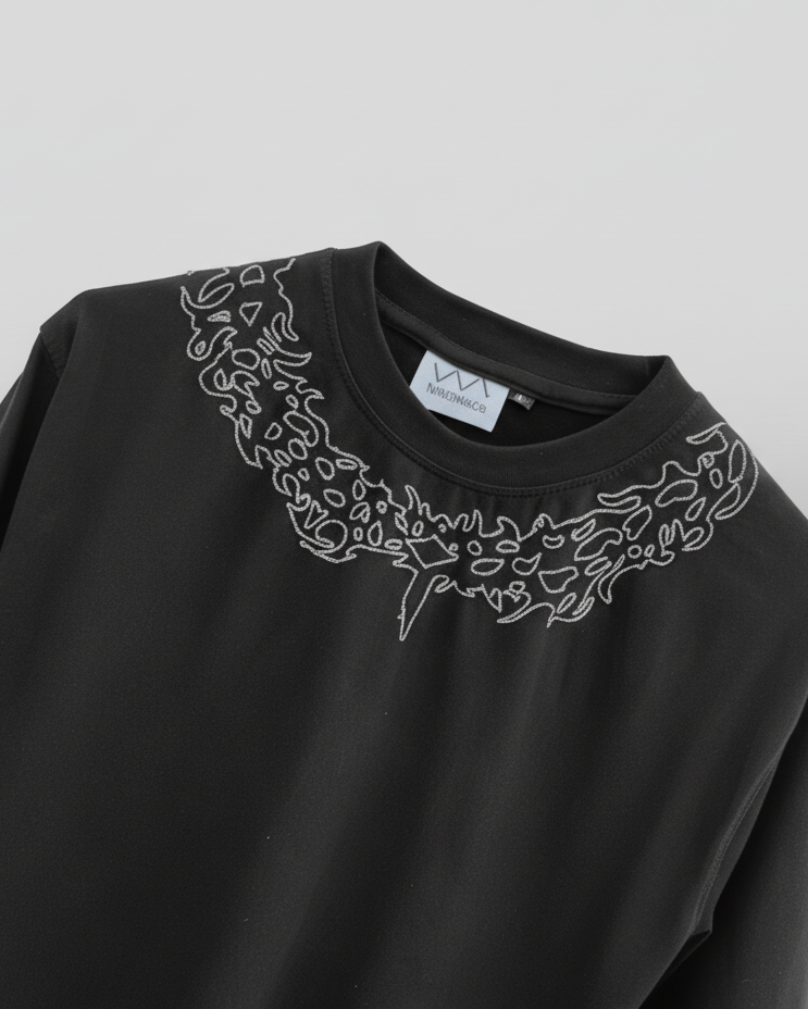 Black tshirt with intricate white embroidery on a gray background