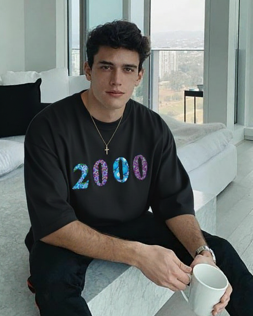 Man wearing a black t-shirt with '2000' design embroidered , sitting in a modern living room.