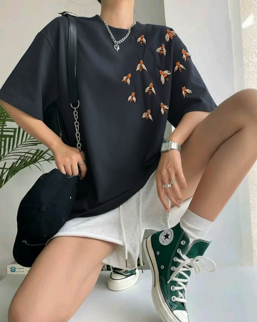 Person wearing a black oversized sweater with orange patterns, white shorts, and green sneakers on a white surface.