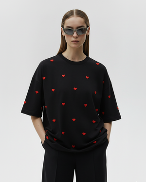 Person wearing a black t-shirt with red heart patterns on a plain background