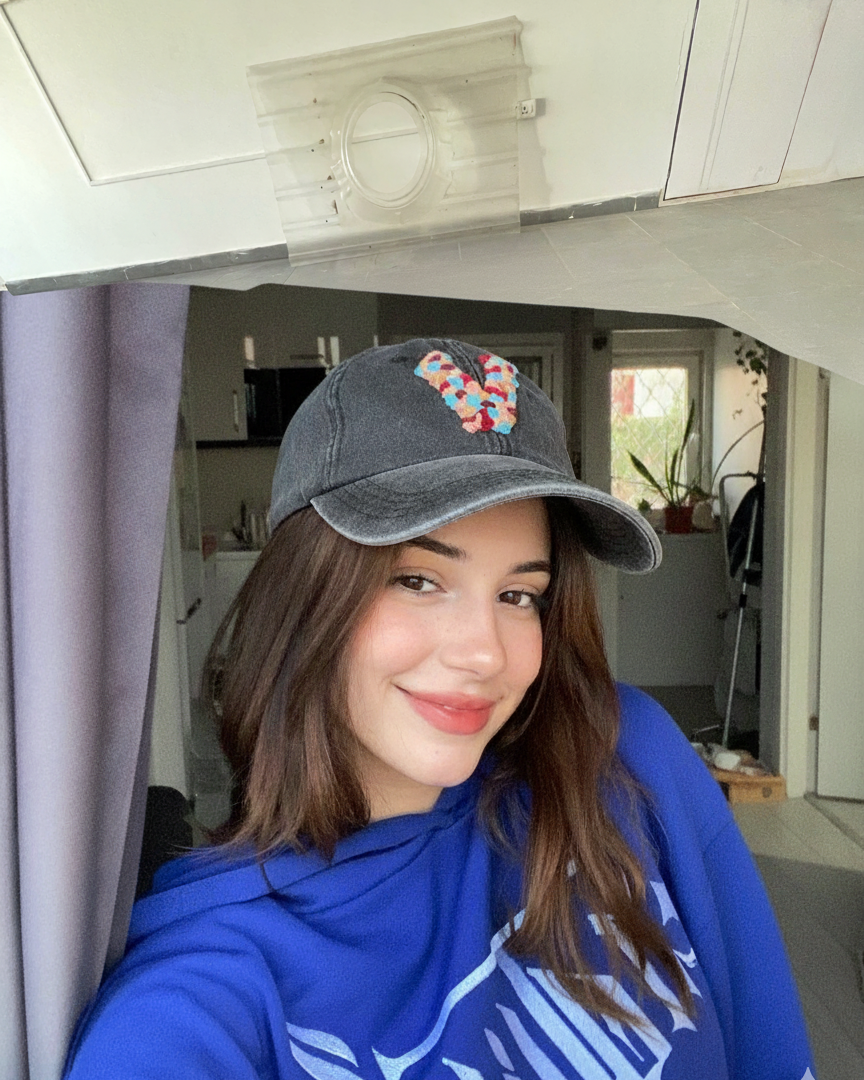 Person wearing a blue hoodie and colorful hand embroidered custom cap inside a vehicle.