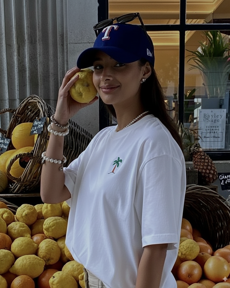 Woman holding a lemon in front of a fruit stand wearing hand embroidered tshirt