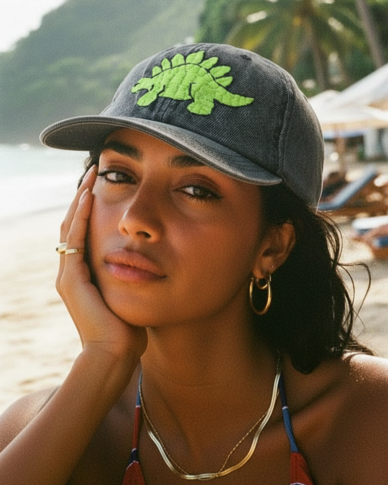 Woman wearing a cap with a green dinosaur embroidered design on a beach