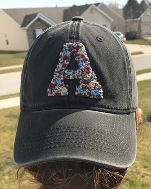 Black cap with floral letter 'A' embroidered on a person outdoors