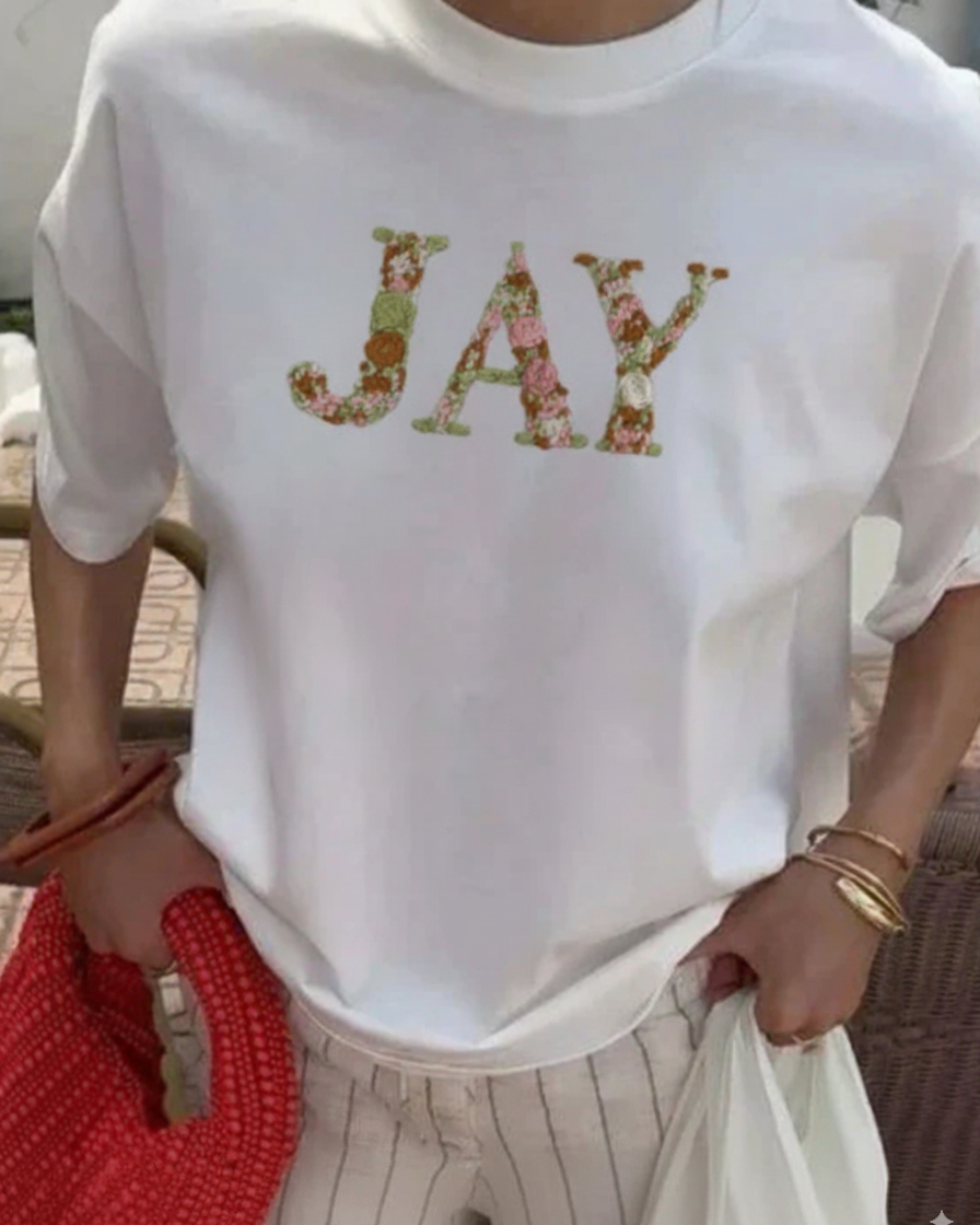Person wearing a white t-shirt with 'JAY' embroidered in colorful letters.