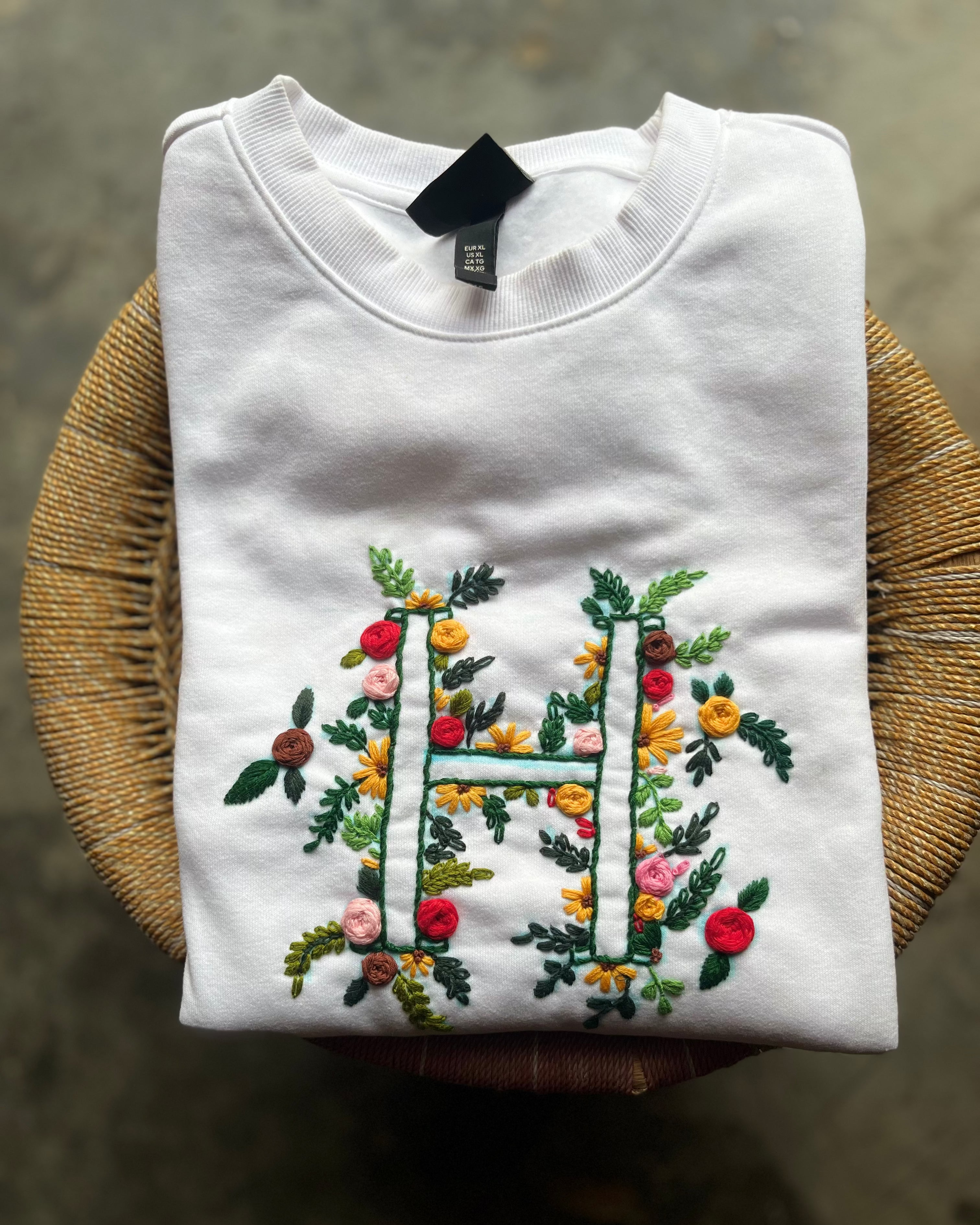 Top view of cream initials sweatshirt with simple ‘h.’ stitching, styled with denim jeans and coffee accessories.