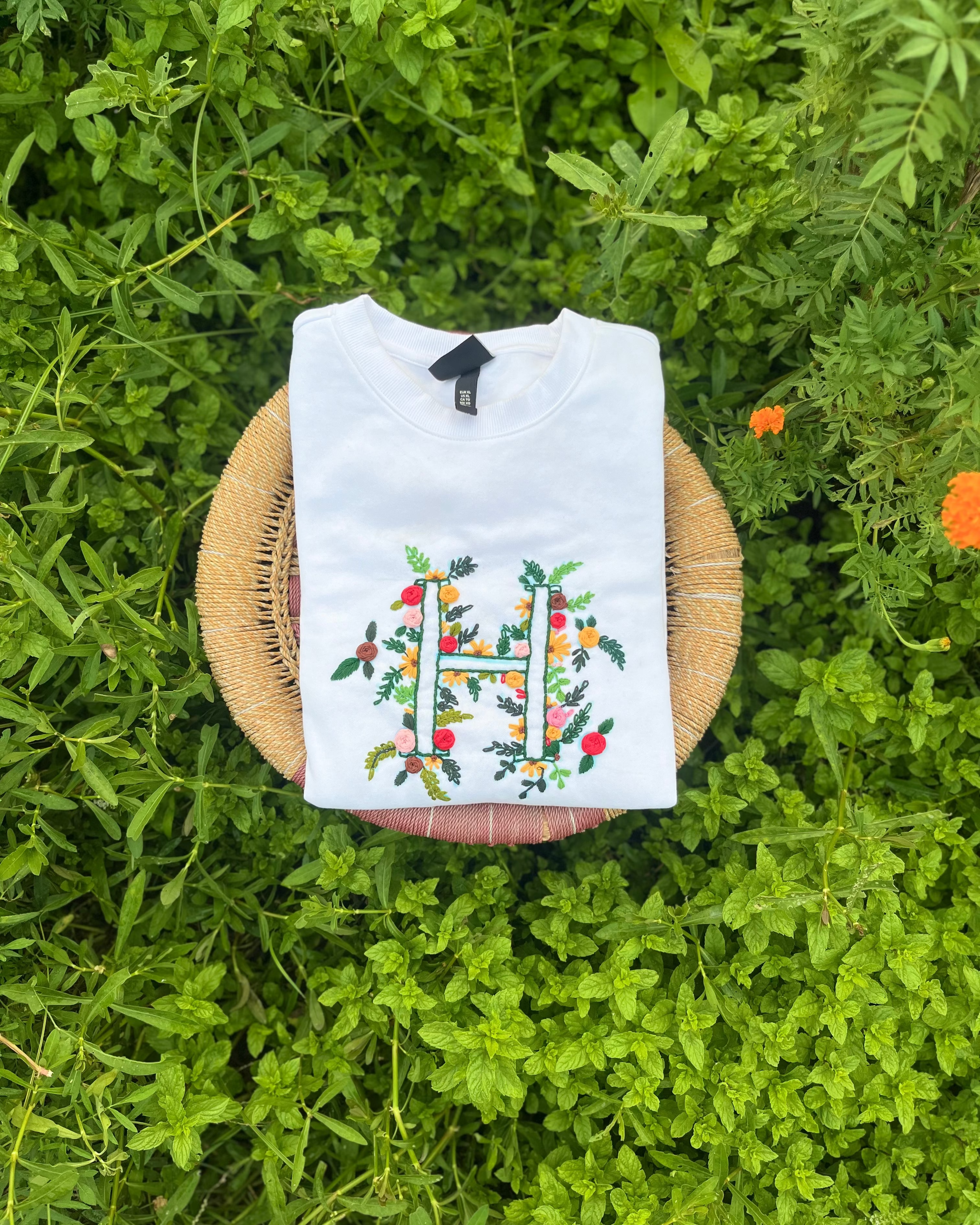 Flatlay of white sweatshirt featuring hand-embroidered initials near the hemline, paired with leather wallet and journal.