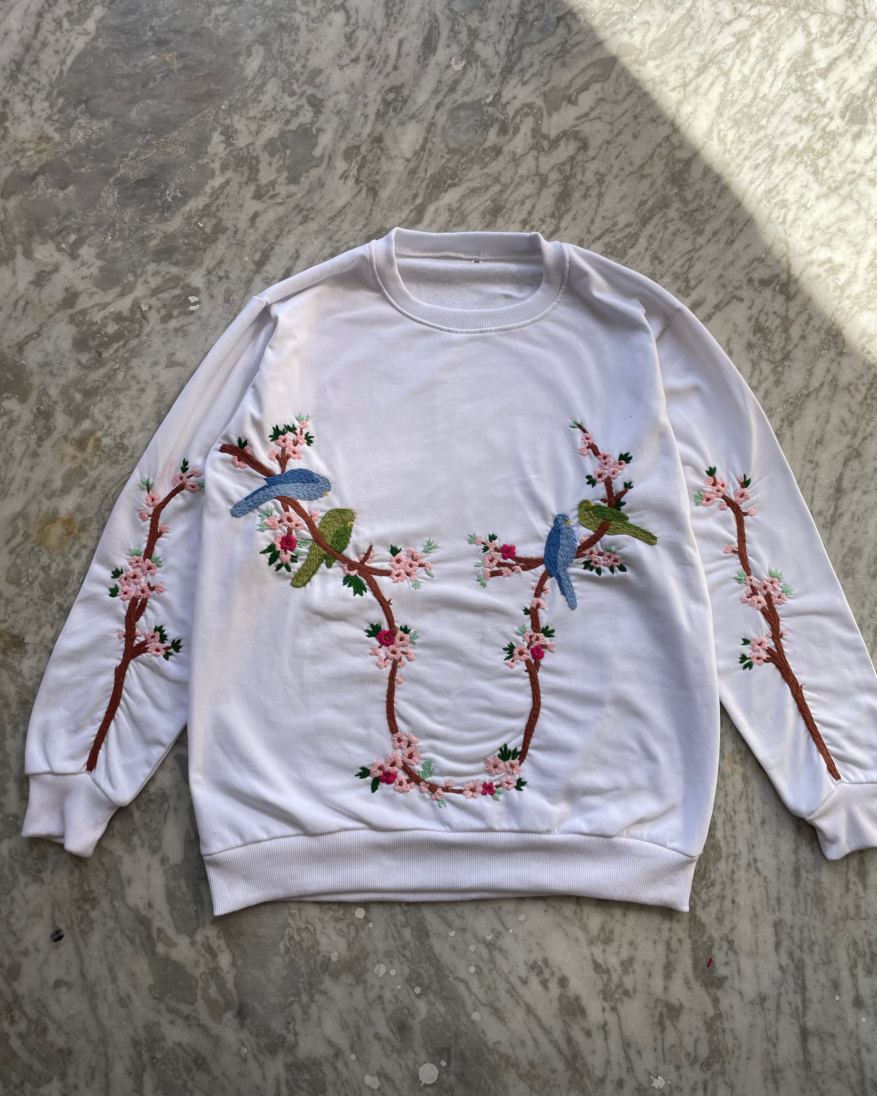 White sweatshirt with floral and bird embroidery on a gray surface