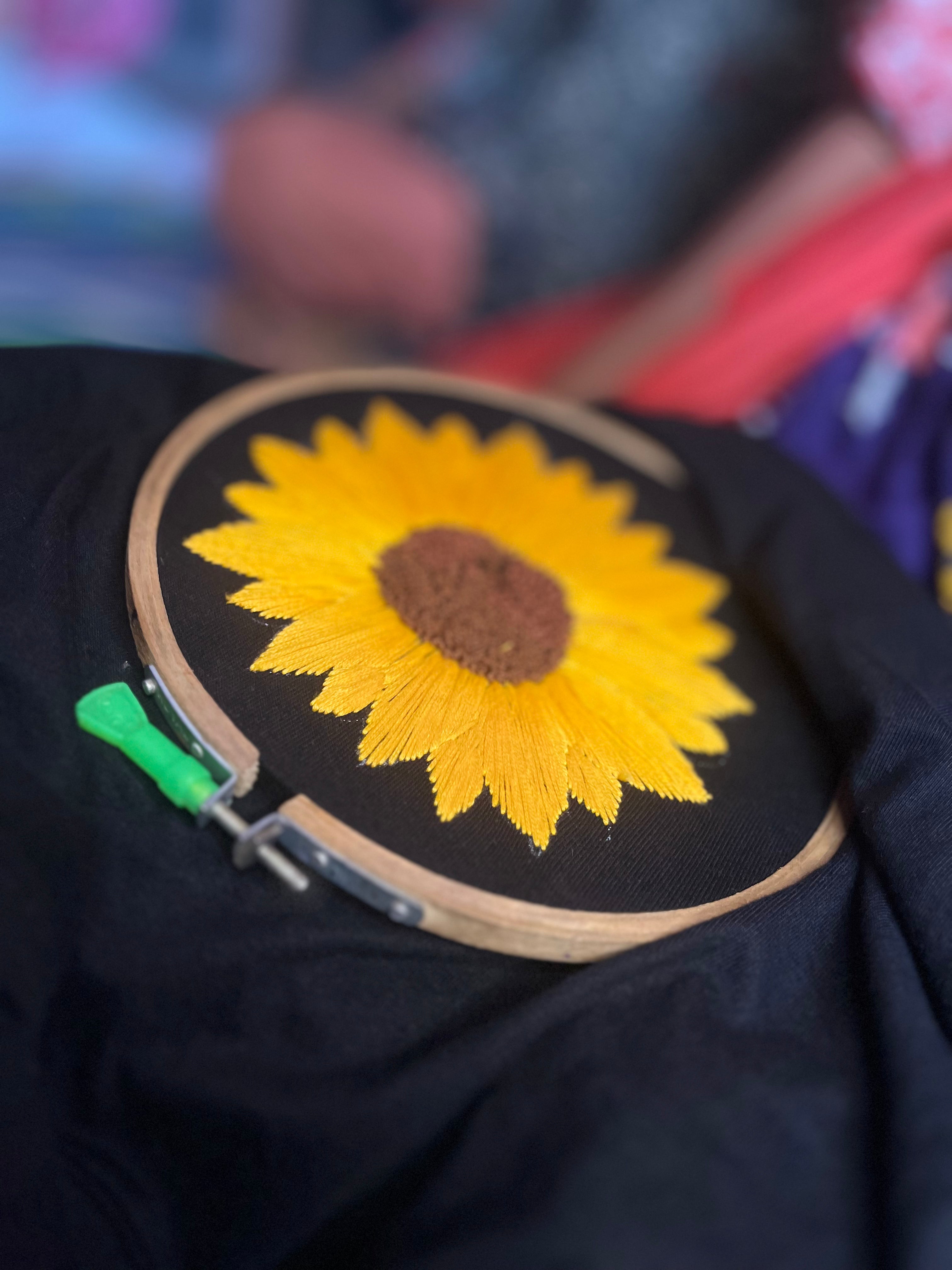 Flat lay showing detailed sunflower hand embroidery on premium cotton tee