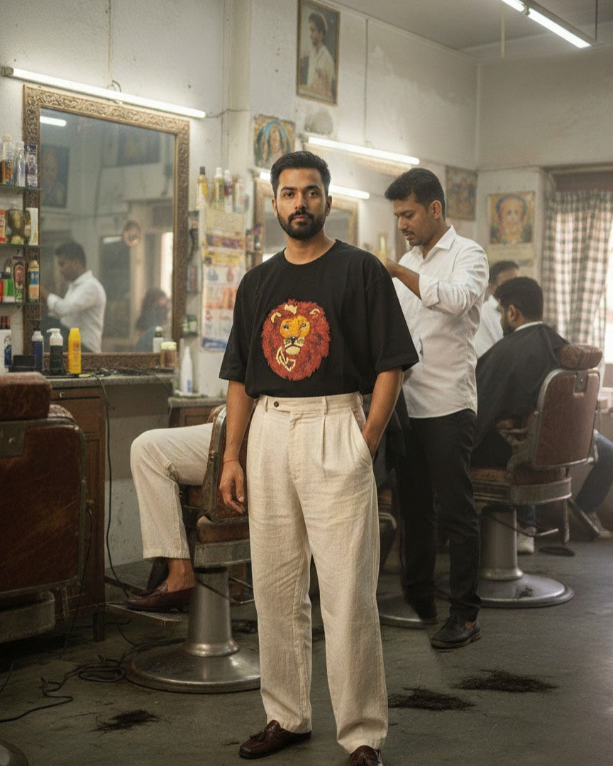 Man wearing a lion embroidered tshirt standing in a barbershop with another man getting a haircut.