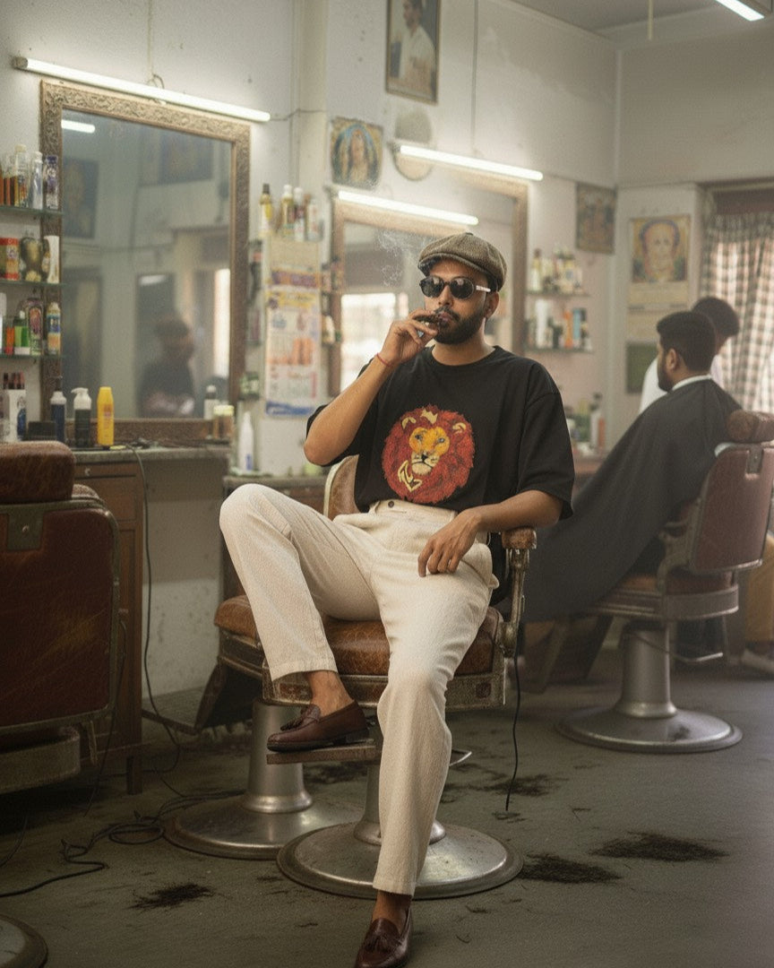 Man sitting in a barber shop chair wearing sunglasses and a black t-shirt with a lion graphic.