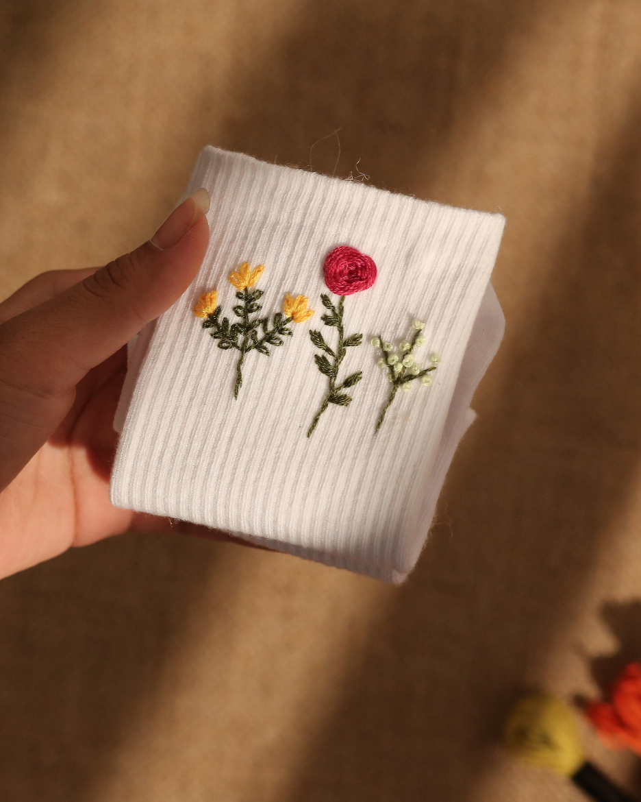 White ribbed knit square with embroidered flowers held by a hand on a beige surface.