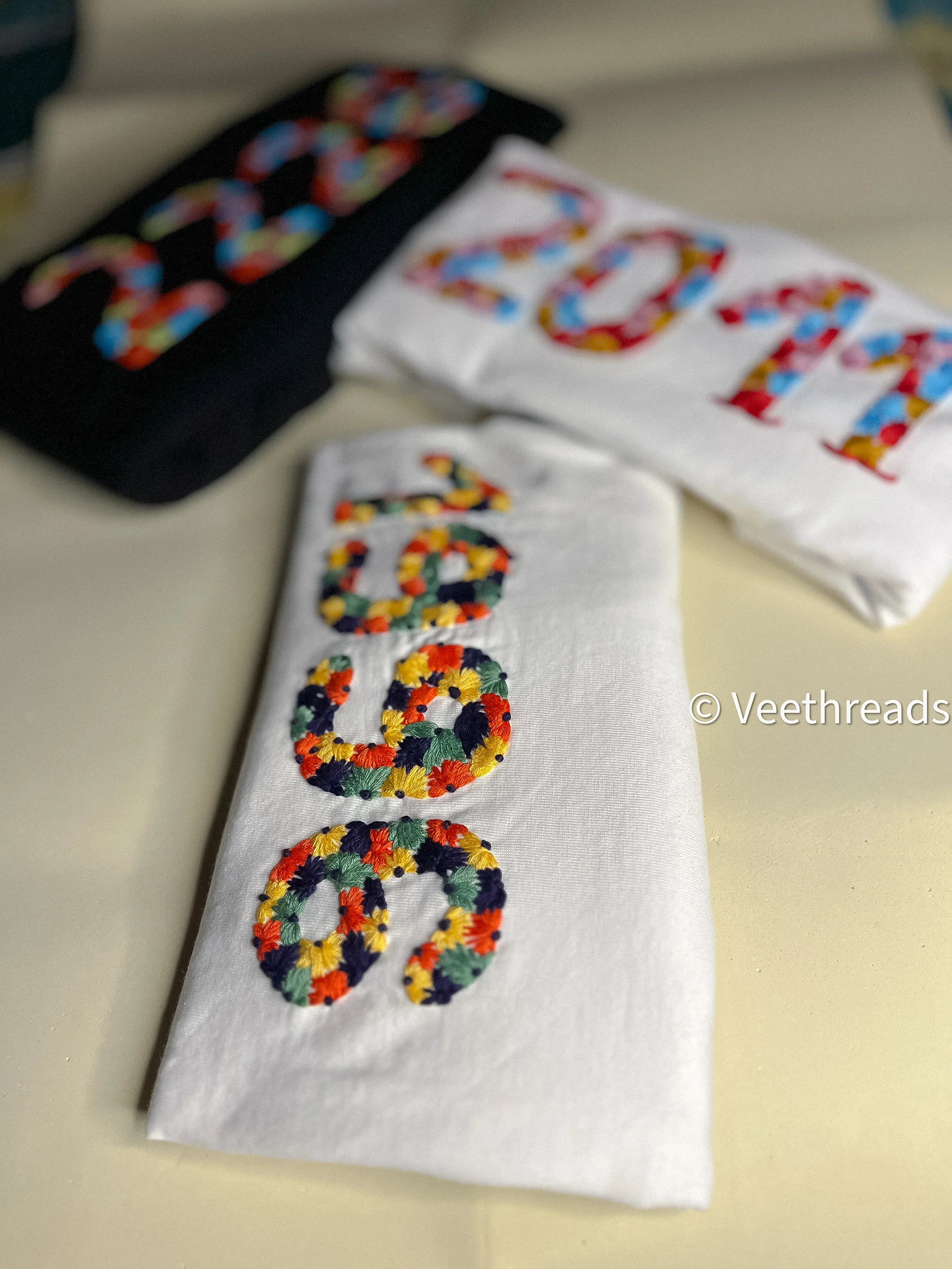 Close-up of hand-stitched year embroidery on a black cotton tee, highlighting clean threadwork.