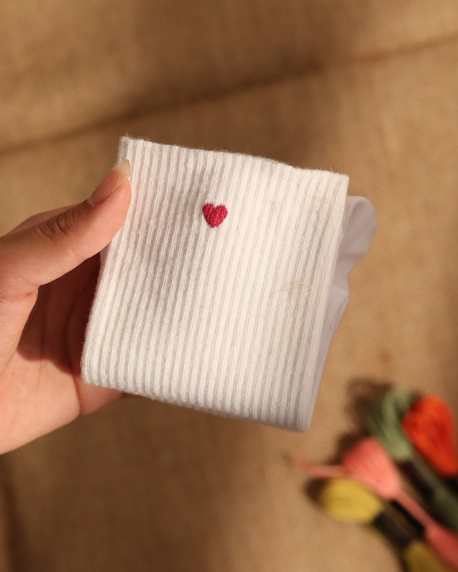 Pair of white cotton socks with red heart embroidery near ankle