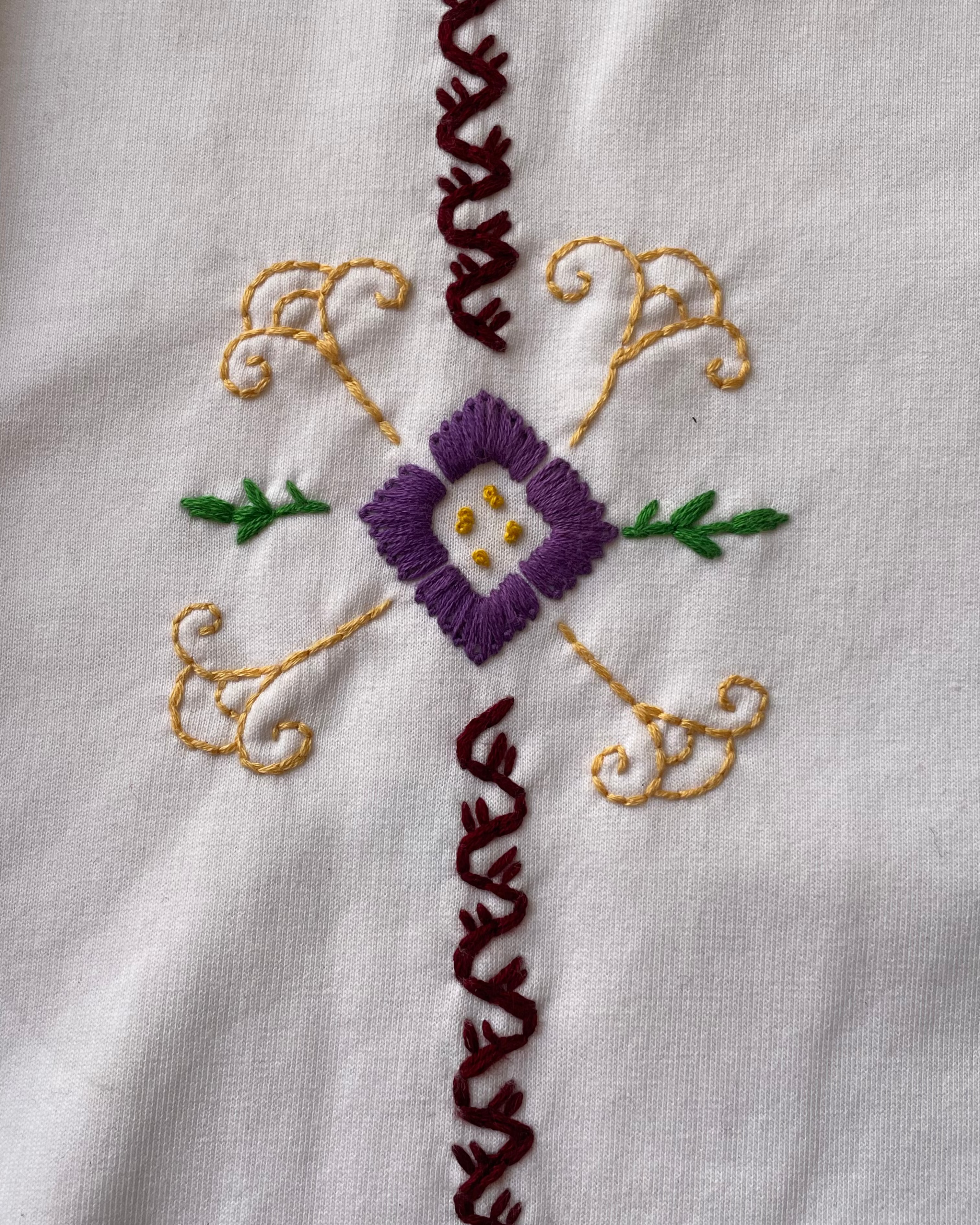 Embroidered design on a white fabric with purple flower and gold leaves.