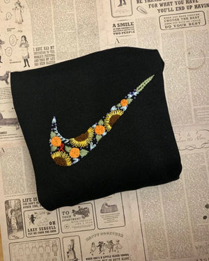 Flatlay of black Nike embroidered t-shirt with swoosh logo near collar, styled with trainers and a water bottle.