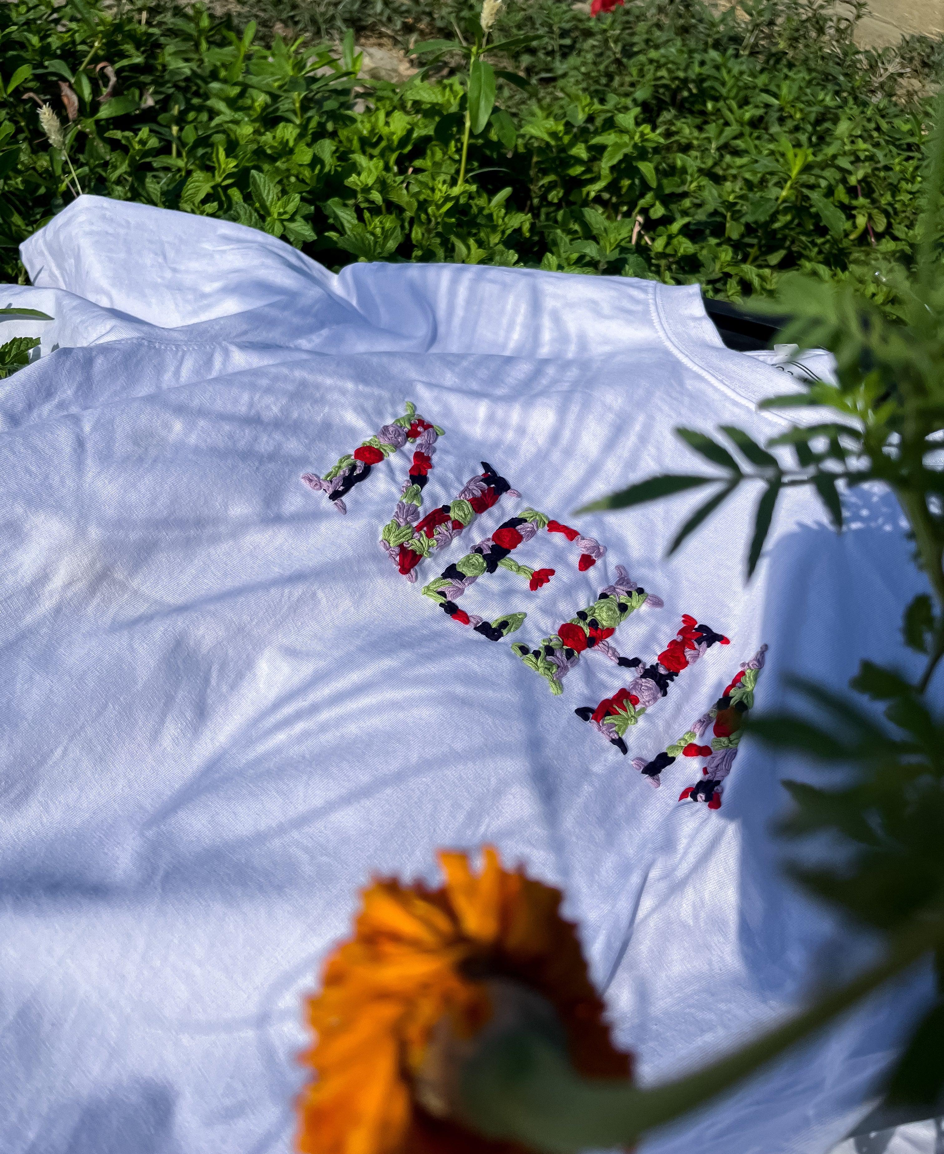 White personalised t-shirt folded neatly with name stitched on the front, placed on a grassy background.