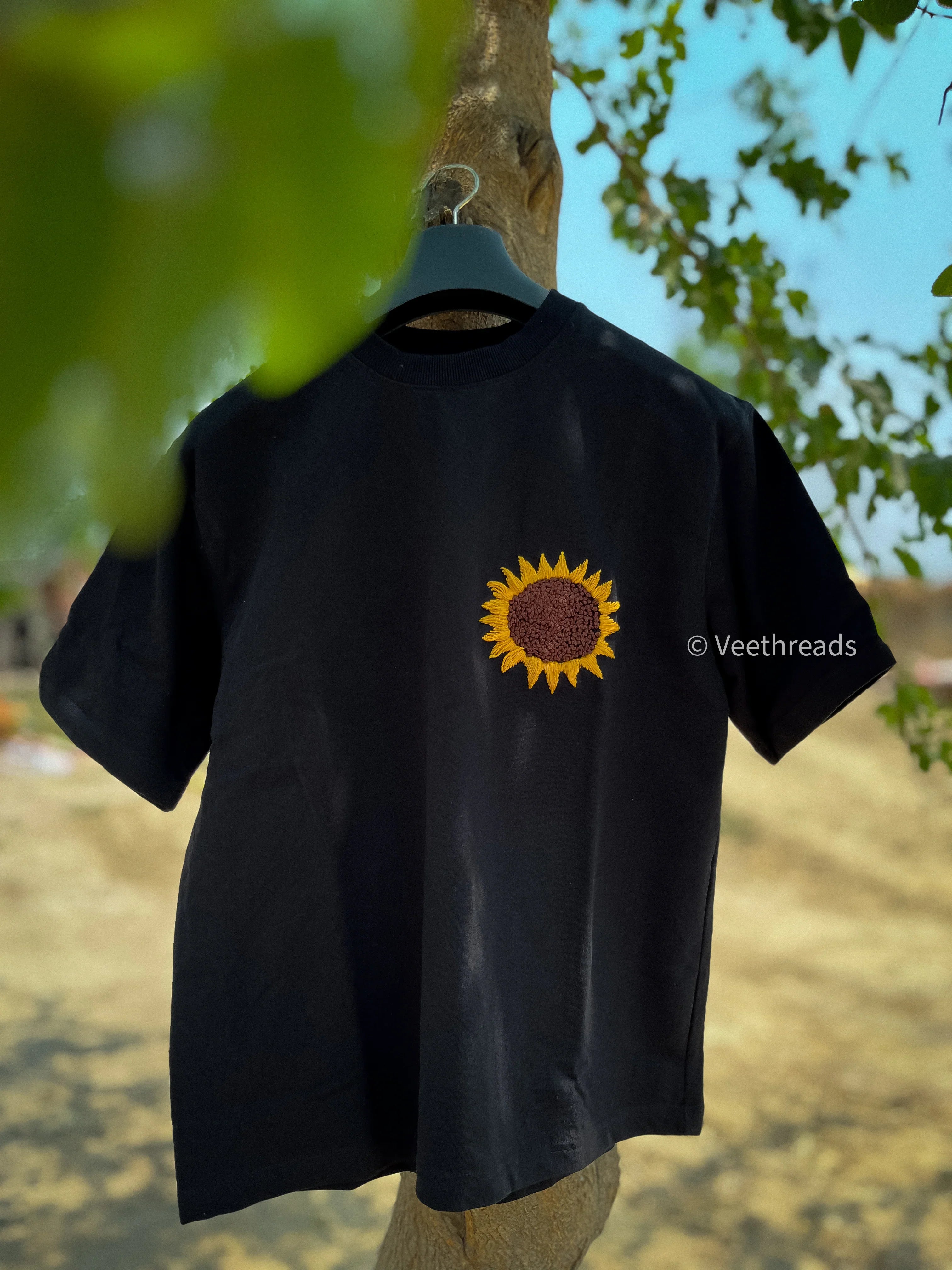 Black t-shirt with a sunflower embroidered on a hanger against a natural background
