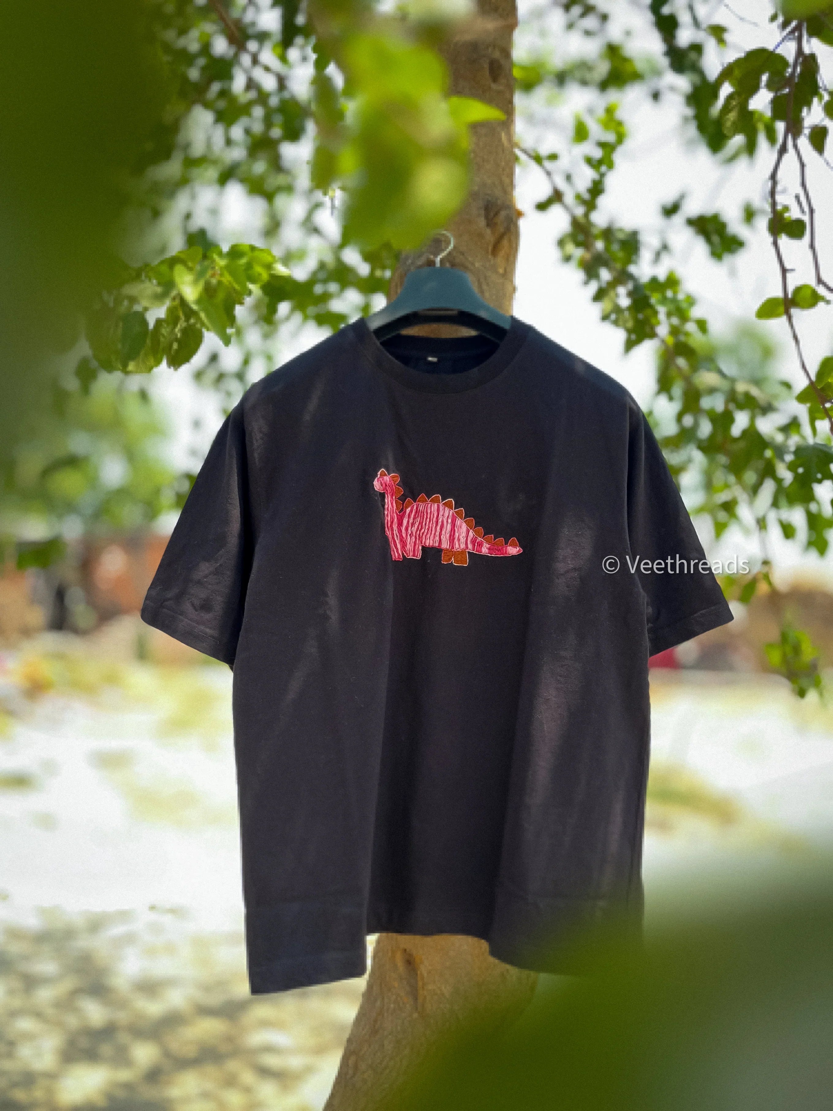 Black t-shirt with red and orange embroidered design on a hanger against a natural background