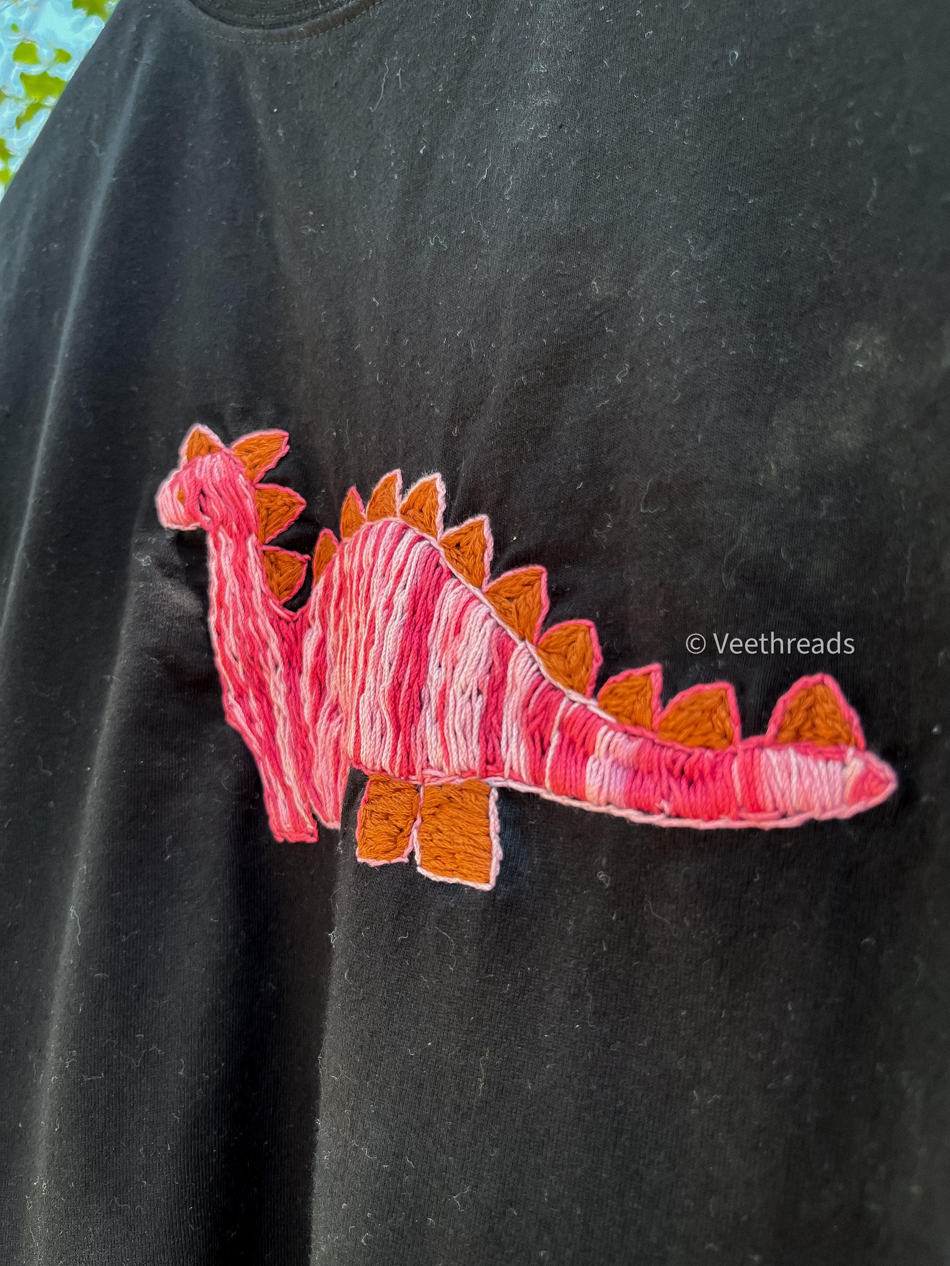 Black t-shirt with a pink and orange dinosaur hand embroidery patch on a dark background