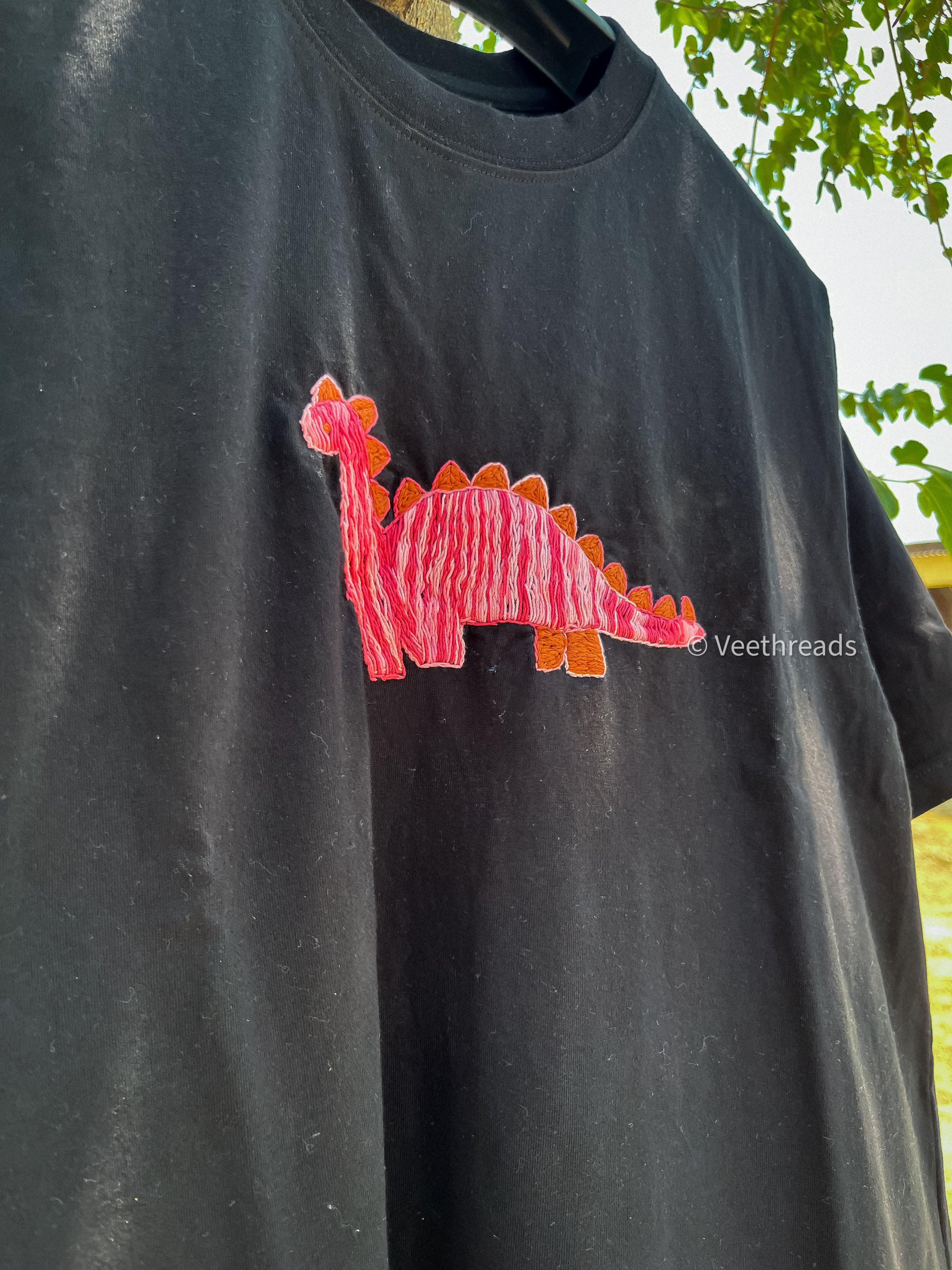 Flat lay of embroidery t-shirt with cute dinosaur stitched on black cotton