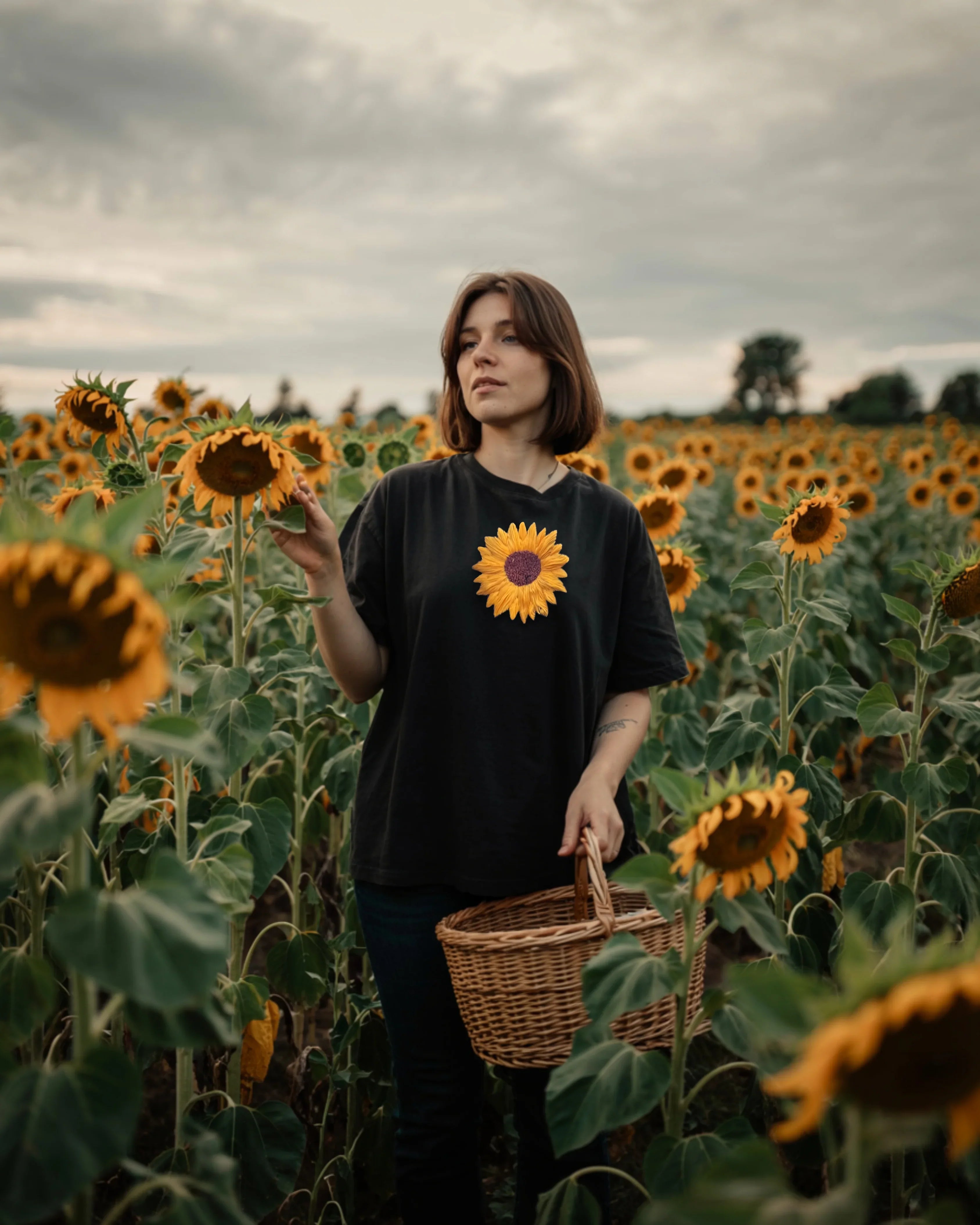 Person standing in a sunflower field wearing a black t-shirt with a Model wearing black oversized t-shirt with sunflower embroidery on chest