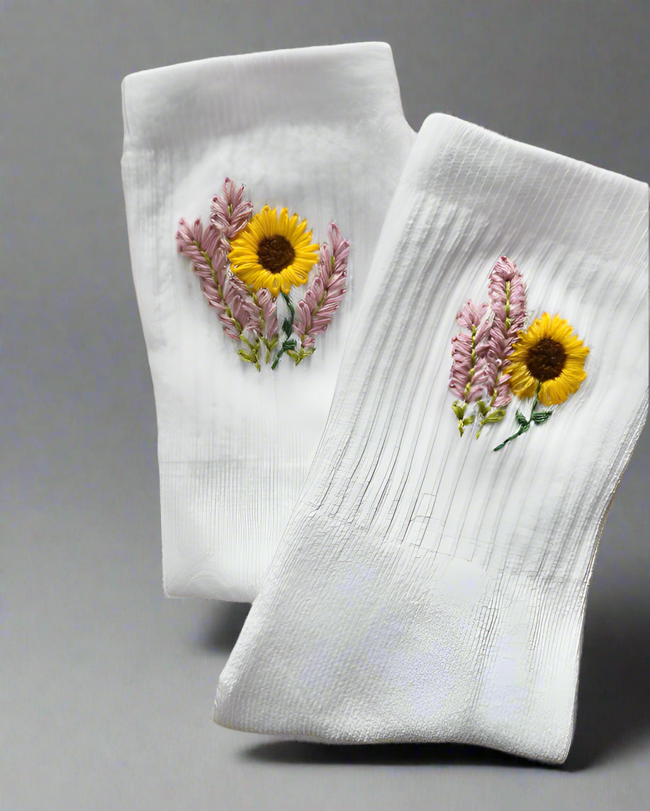A pair of white socks with hand embroidery designs that include sunflowers and lavender.