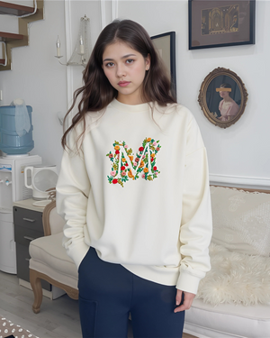 Young woman smiling while wearing a soft beige sweatshirt with stitched initials on the sleeve, styled in natural lighting.