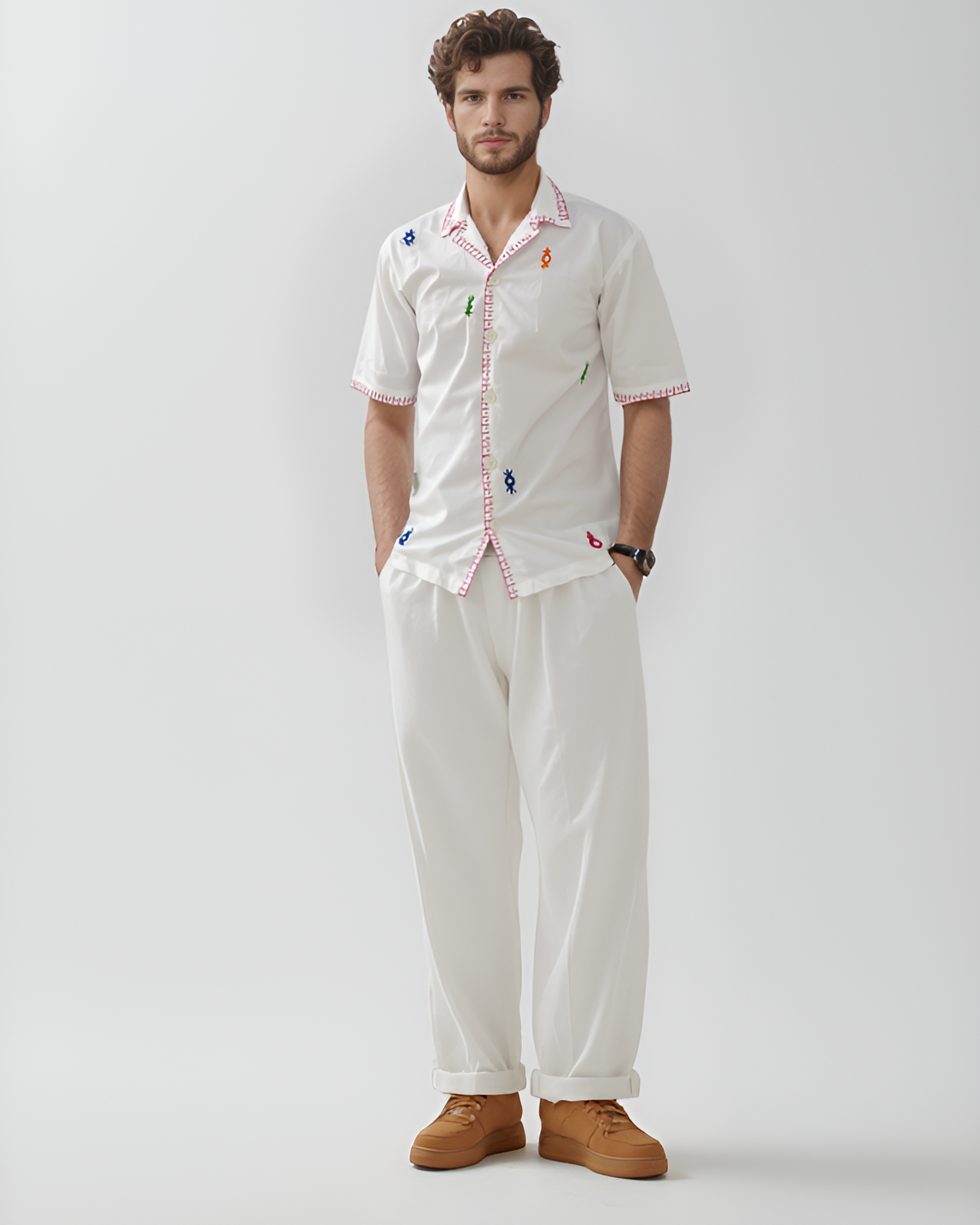 Man wearing a white shirt with colorful mirror work patterns and white pants on a plain background