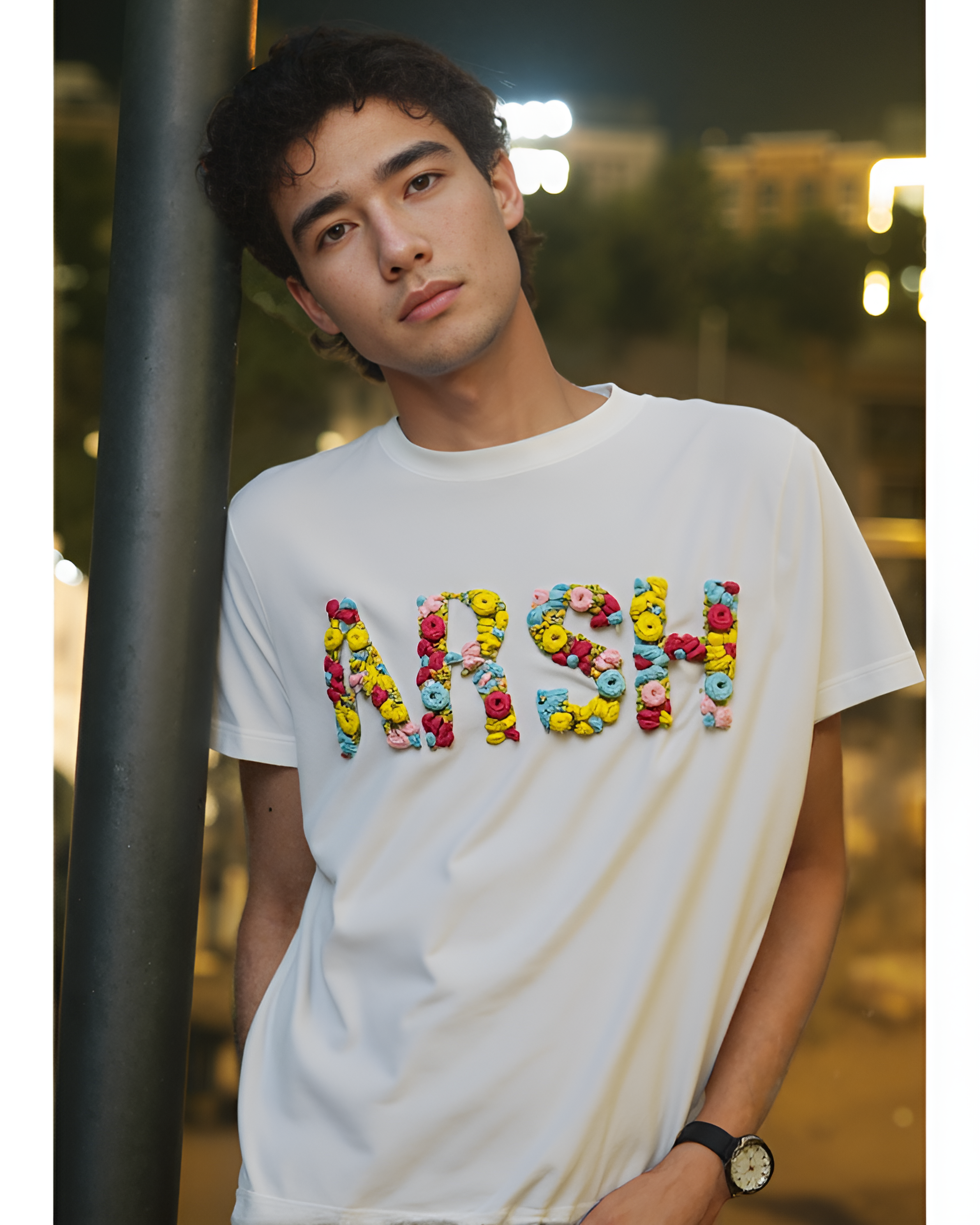 Person wearing a white t-shirt with custom name embrodiered in colorful text, standing outdoors at night.