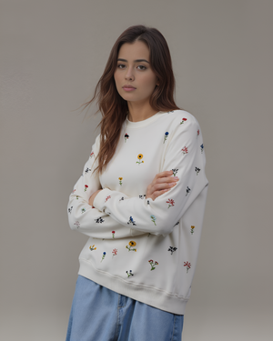 Woman wearing a white sweatshirt with floral embroidery against a plain background