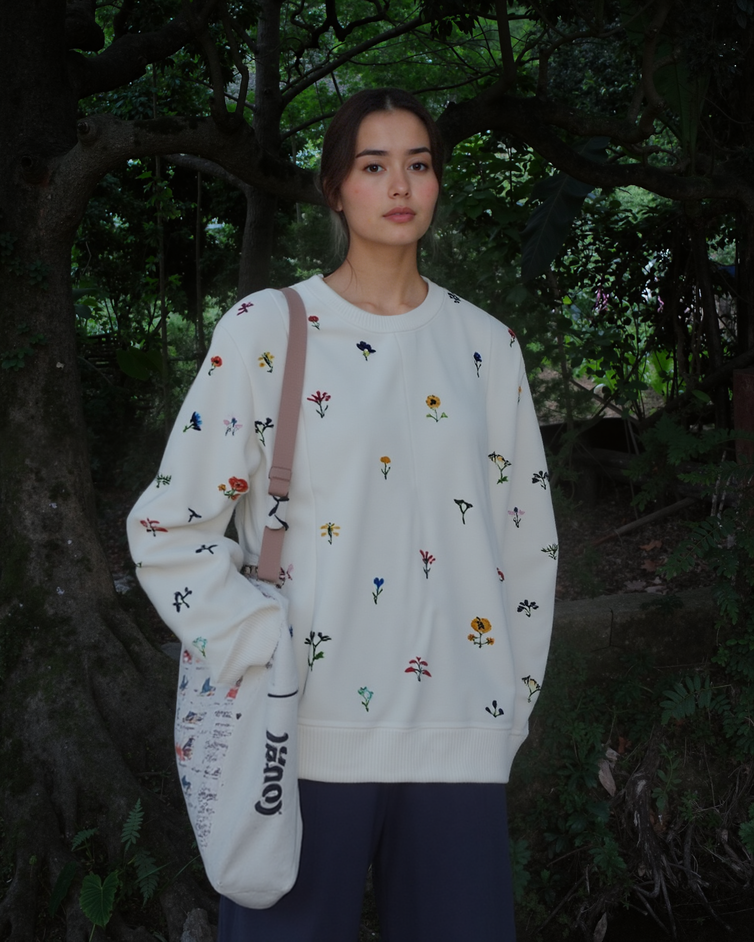 Person wearing a white sweater with floral embroidered patterns in a forest setting