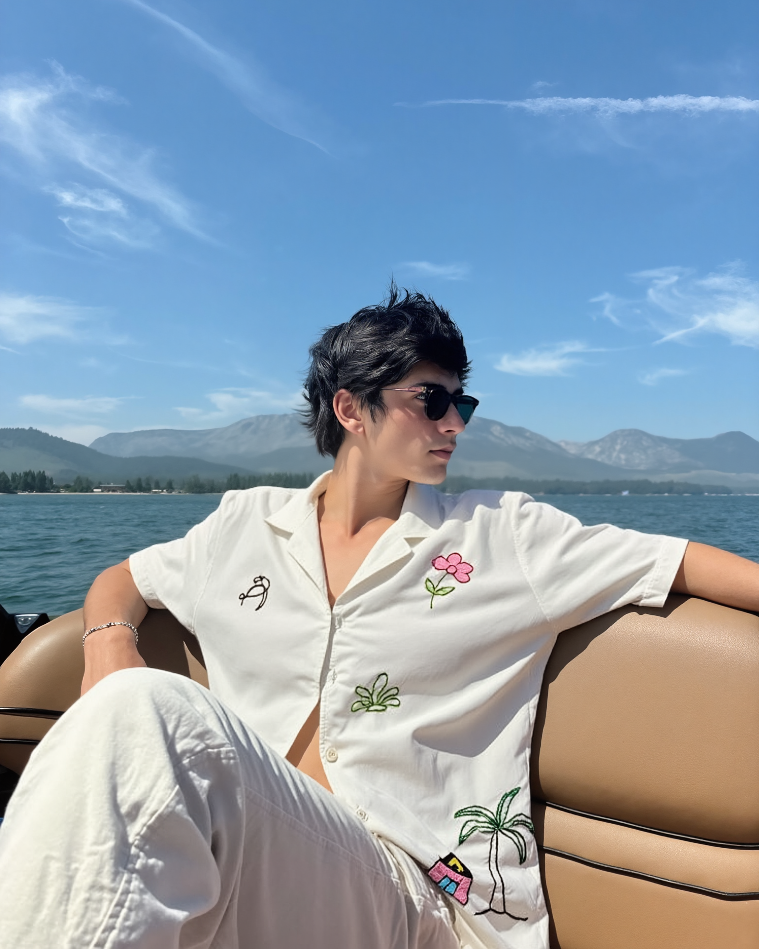 Person sitting on a boat with a scenic background of mountains and blue wearing hand embroidered shirt sky.