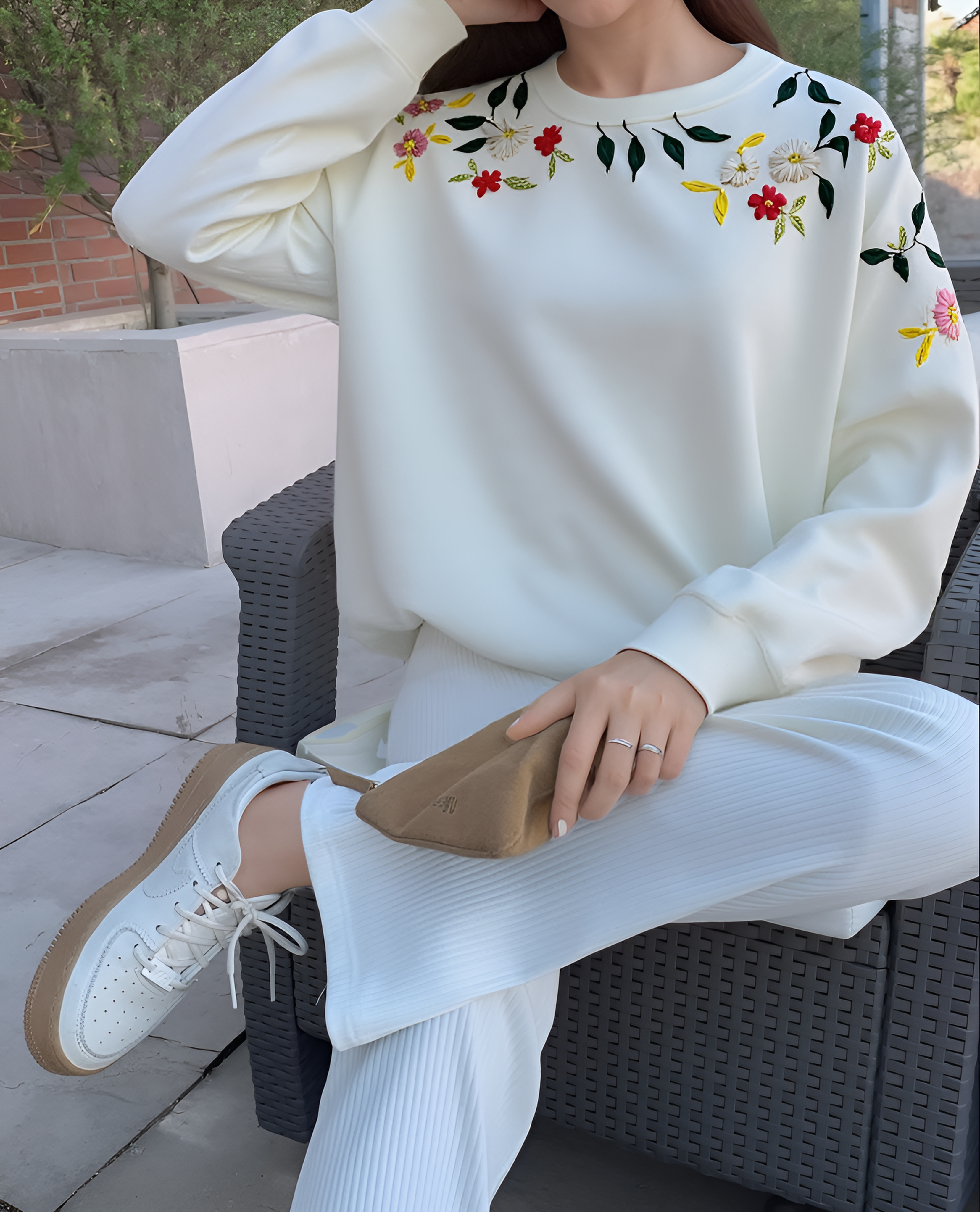 Person wearing a white sweatshirt with floral embroidery sitting on outdoor furniture.