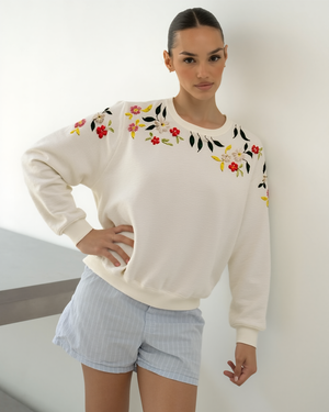 Woman wearing a cream sweater with floral embroidery against a white background