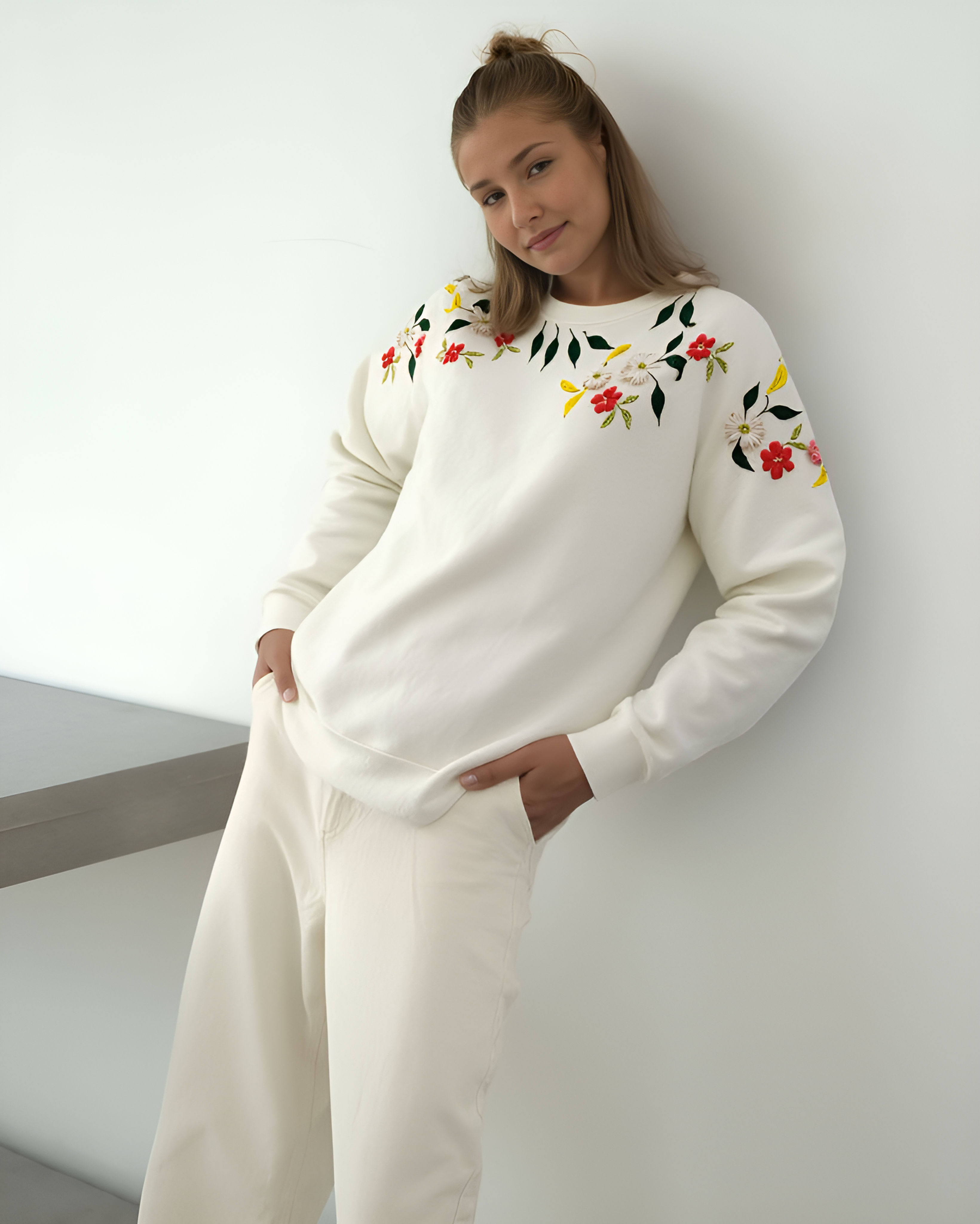 Woman wearing a white sweater with floral embroidery against a plain background