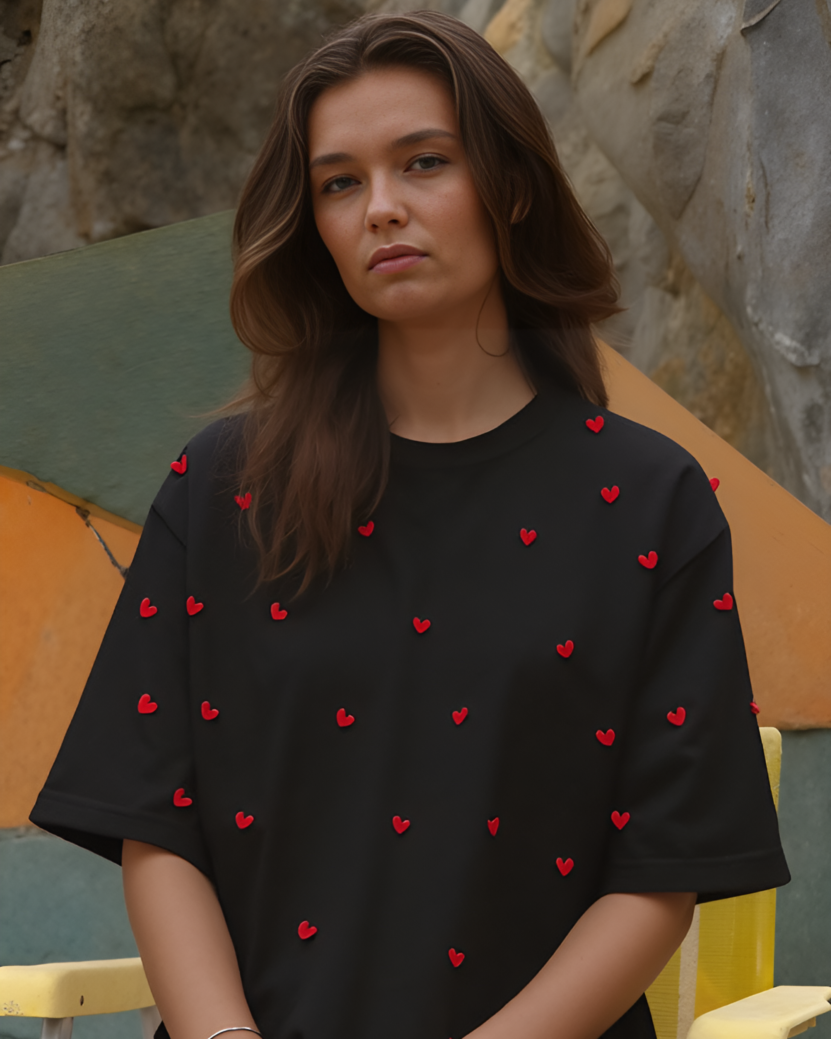 Woman wearing a black t-shirt with red heart patterns sitting against a stone wall.