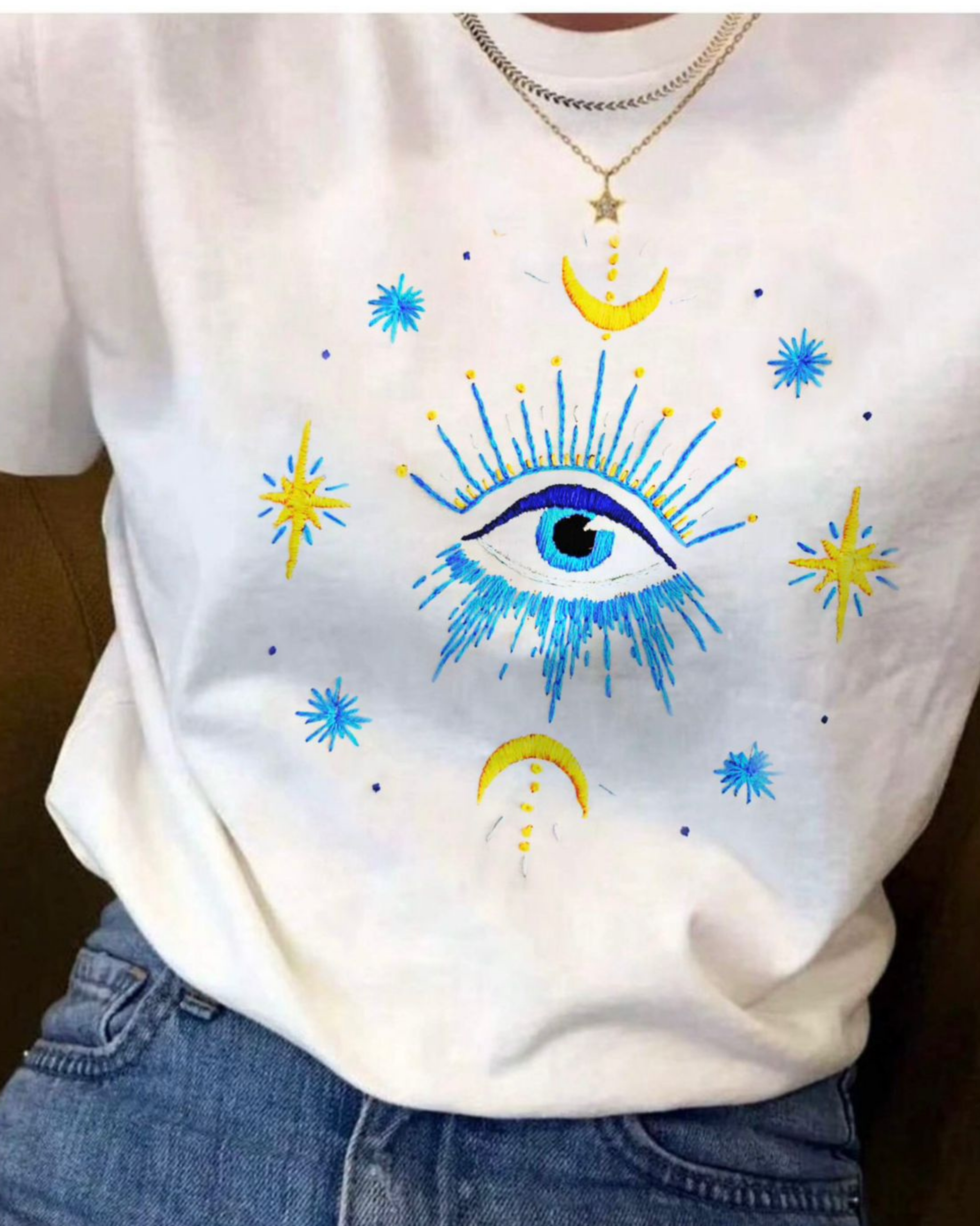 White sweatshirt with blue evil eye design embroirded and colorful stars and moons on a white background
