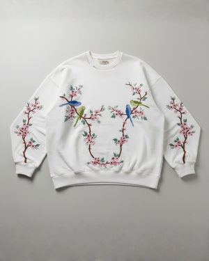 White sweatshirt with floral and bird designs han dembroidery on a gray background